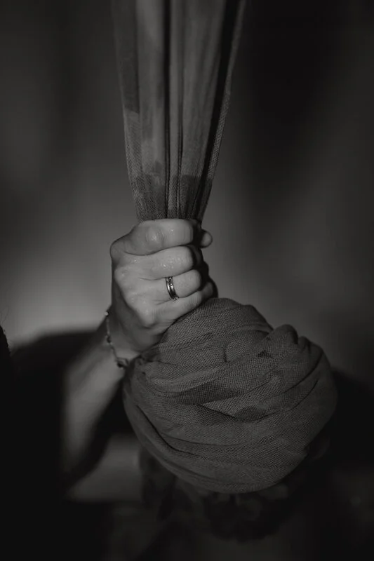 Man sieht auf dem schwarz weiß Foto einen Ausschnitt einer Geburtsszene. Nahaufnahme einer Hand, die sich an einem Seil festhält, welches über einer Gebärwanne hängt.