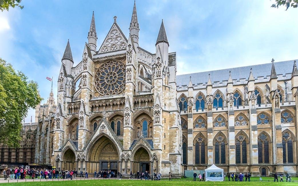 The Gothic-style Westminster Abbey church with intricate architectural details and a large circular stained glass window, with visitors gathering outside.