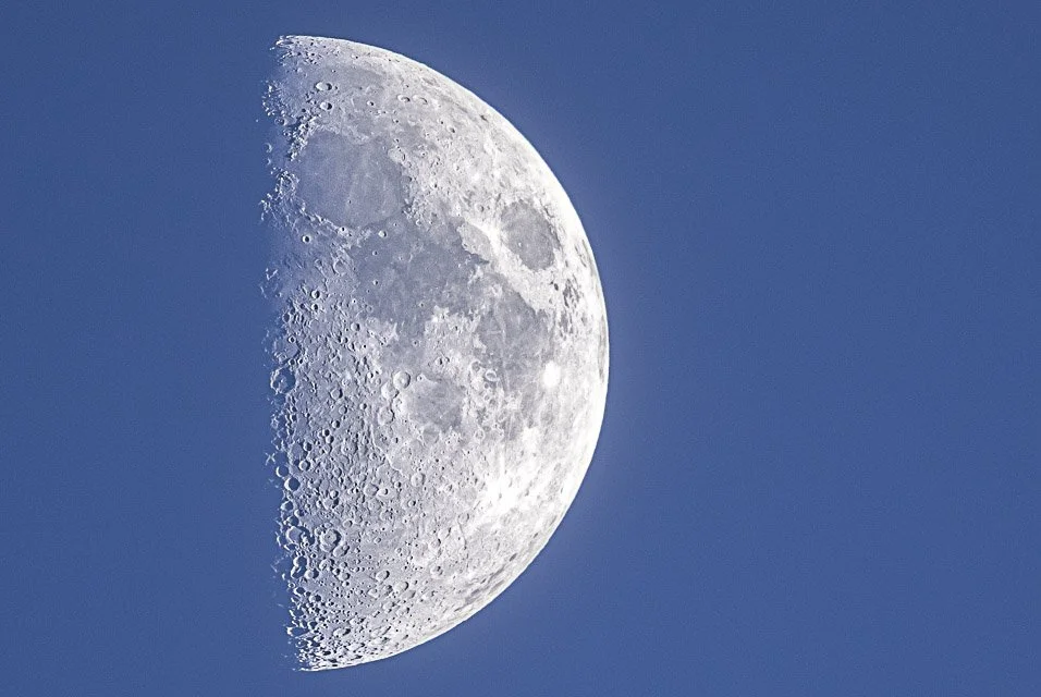 Close-up of the moon in a clear blue sky, showing its craters and surface details.