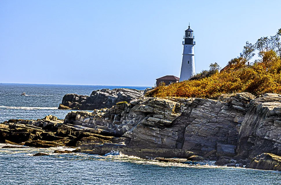 A lighthouse perched on rocky cliffs overlooking the sea with a boat passing in the water.