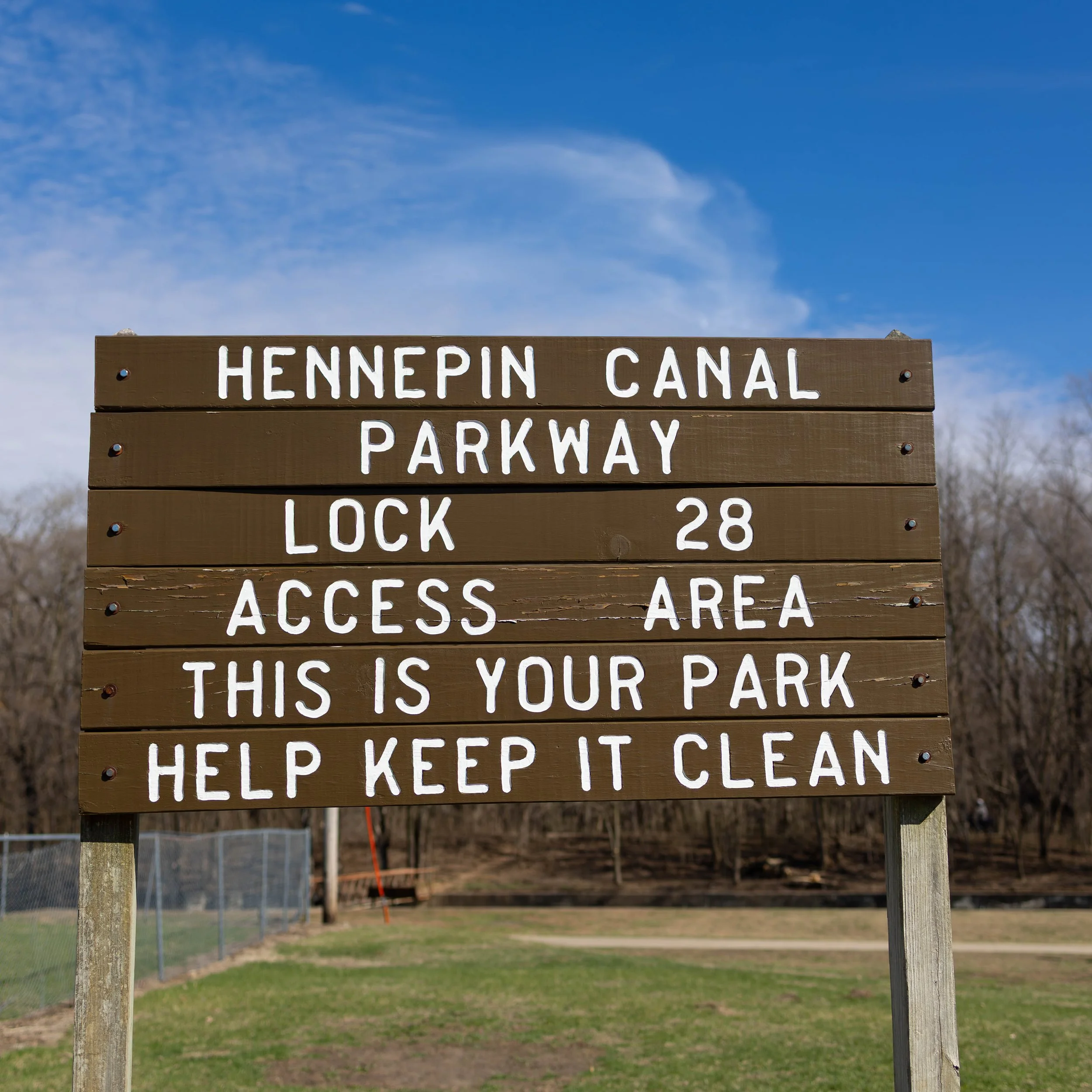 Brown informational sign with white painted text indicating the Hennepin Canal Parkway Lock 28 access area, asking visitors to help keep it clean.