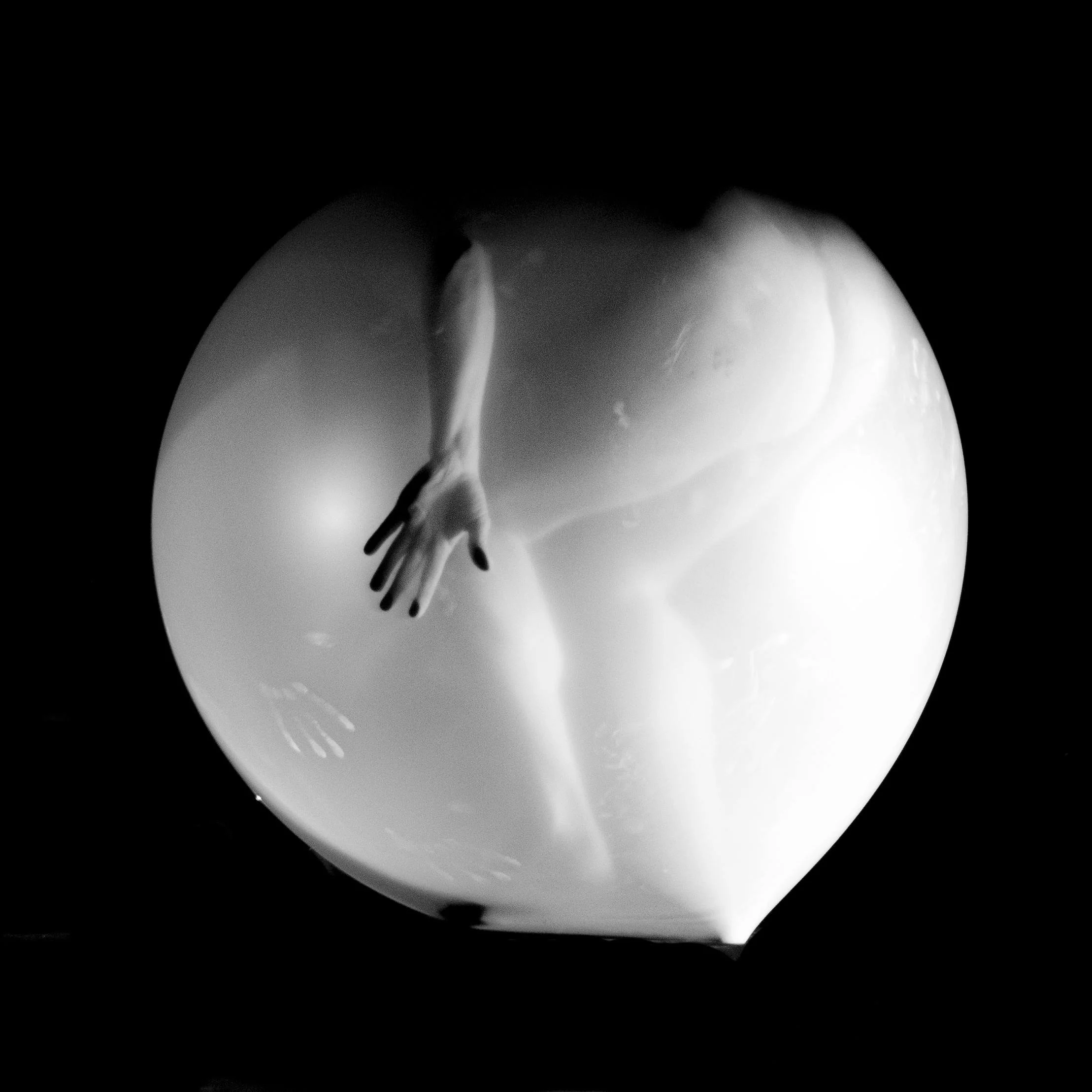 Black and white photo of an arm and hand reaching out through a cut in a large, spherical object.