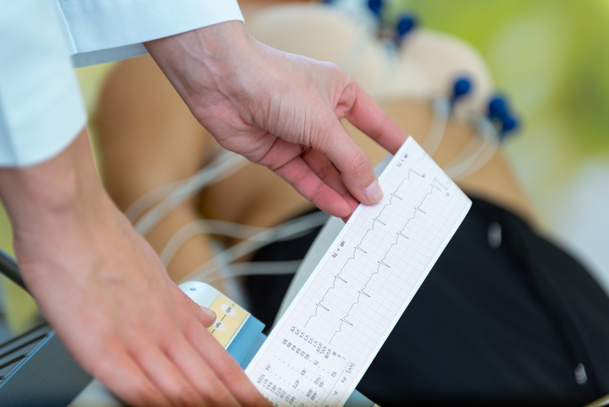 Un medico tiene in mano un foglietto con un elettrocardiogramma, mentre sfiora una macchina per analisi.