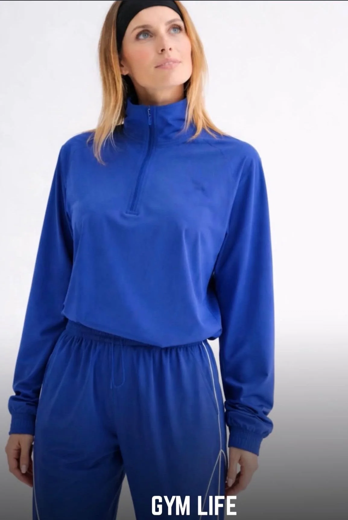 Woman in blue gym outfit with high zip jacket and matching pants.