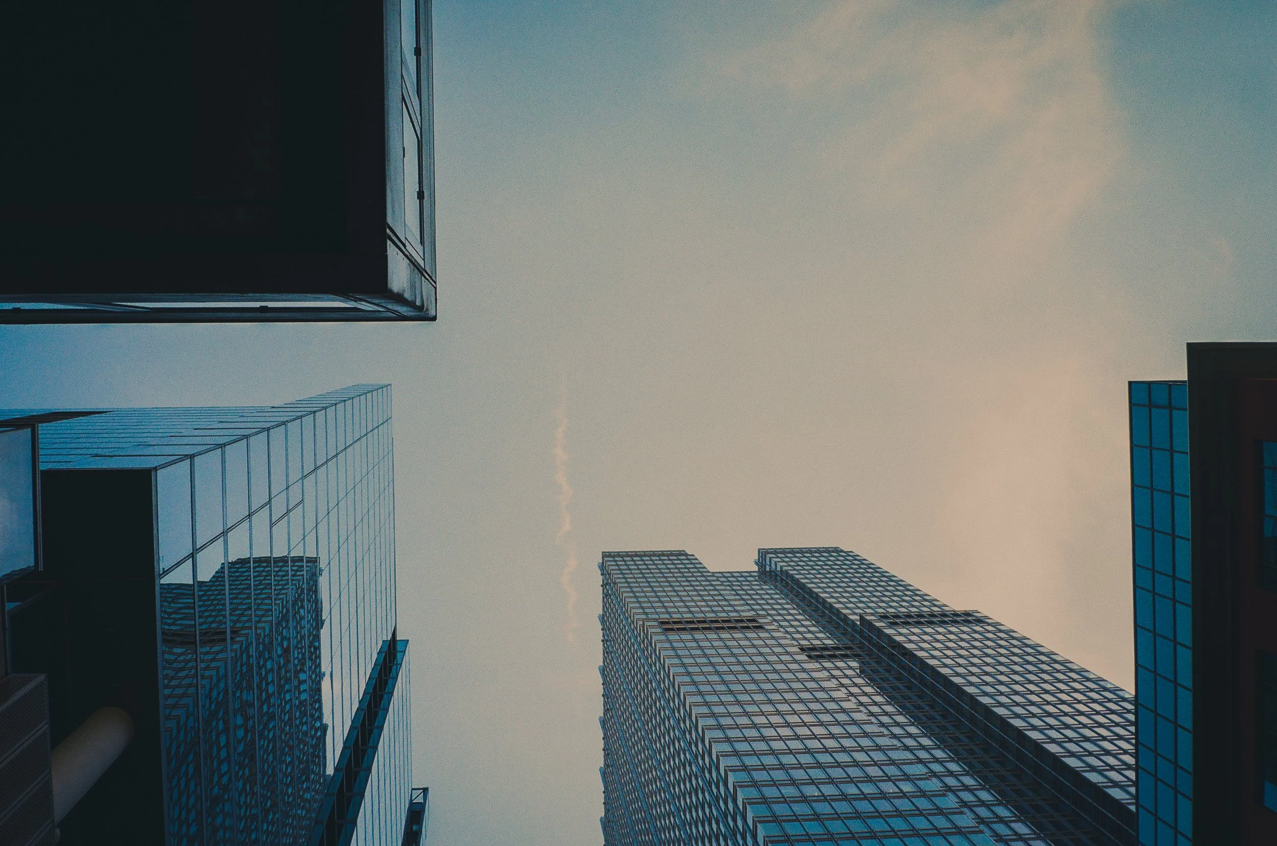 View looking up at tall skyscrapers with glass facades against a blue sky with a few wispy clouds.