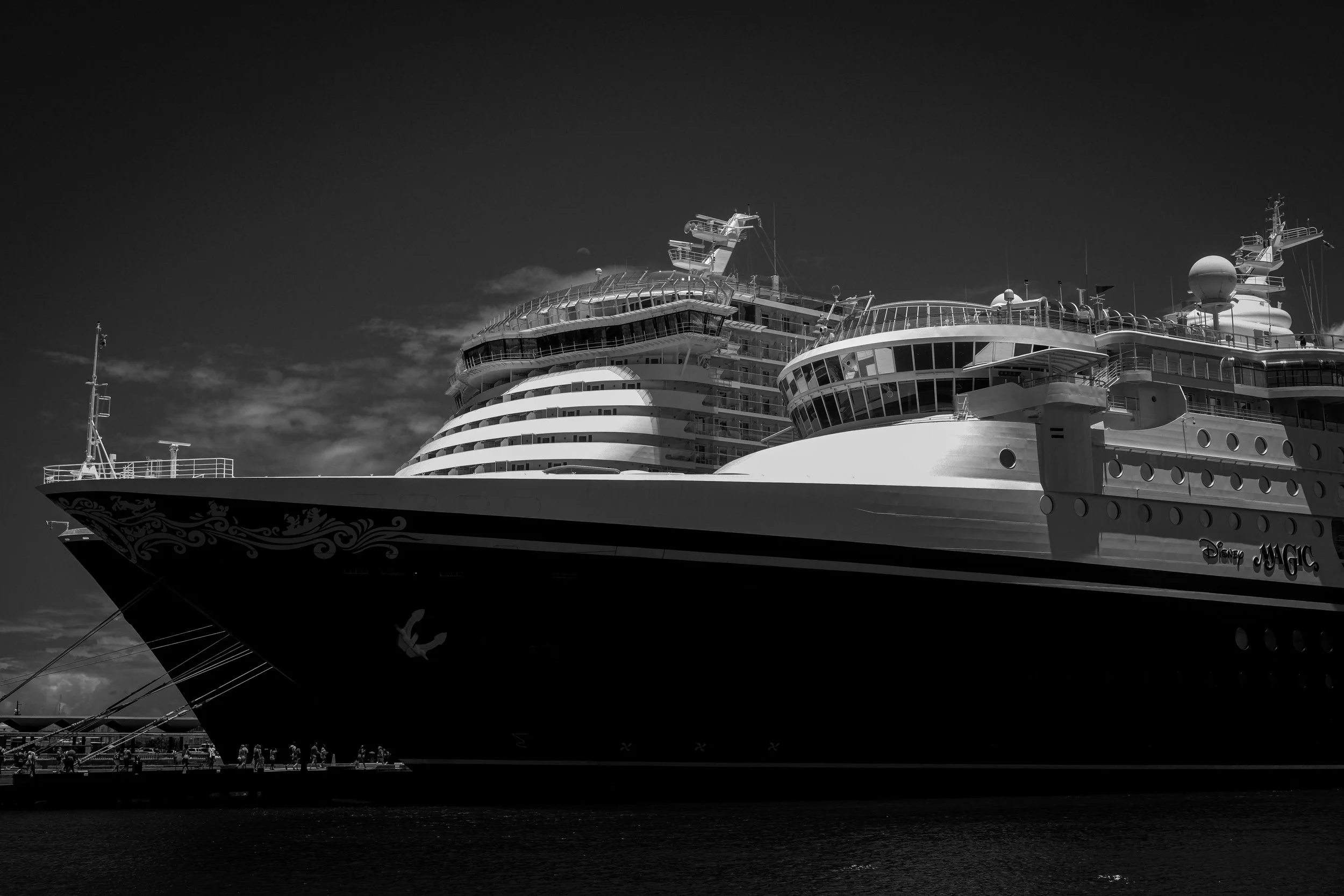 Black and white photo of a Disney cruise ship docked at a port, with the ship's name 'Disney Magic' visible on the side.