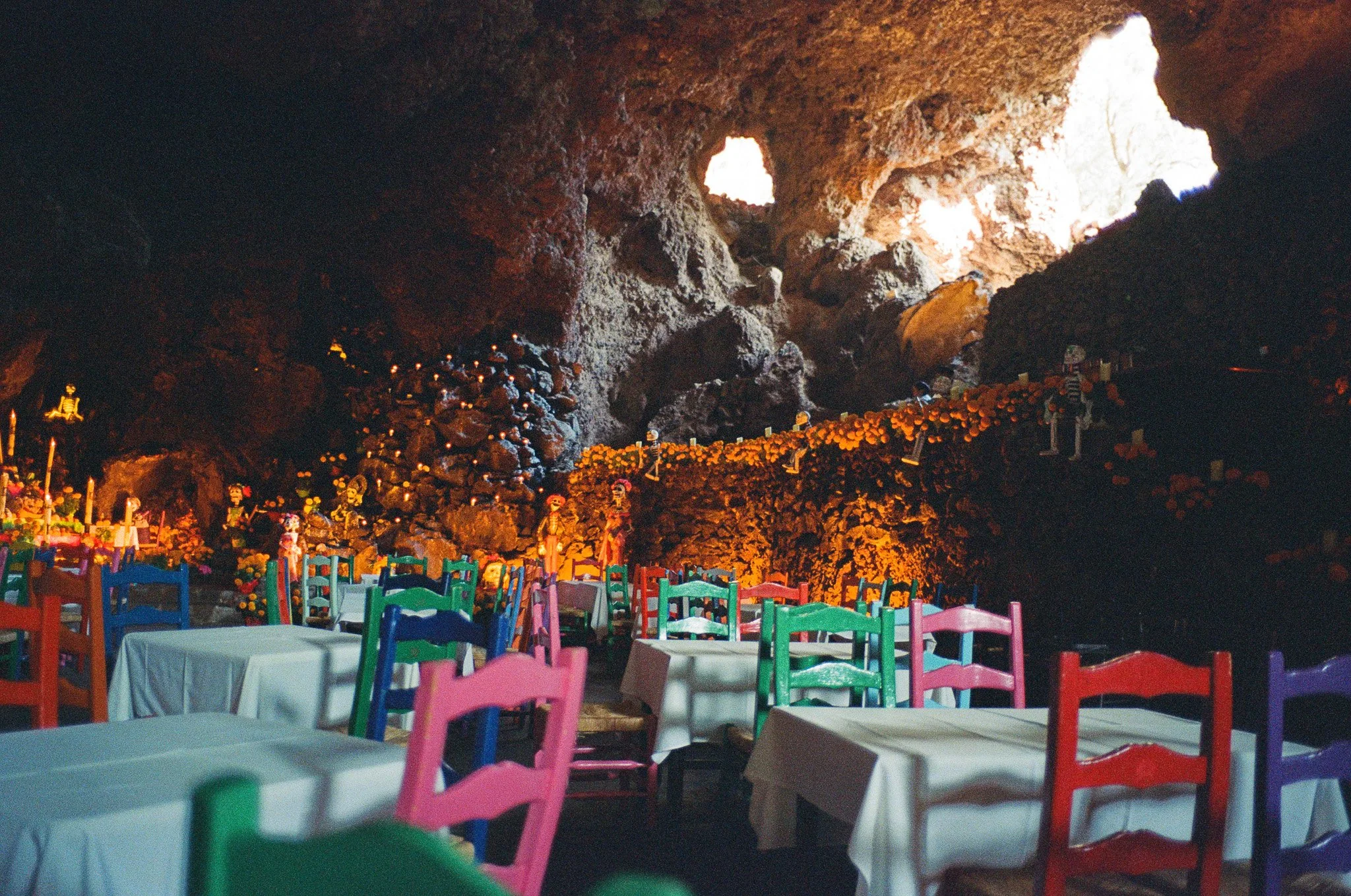 A restaurant interior in a cave with colorful chairs, white tablecloth-covered tables, and Halloween decorations.