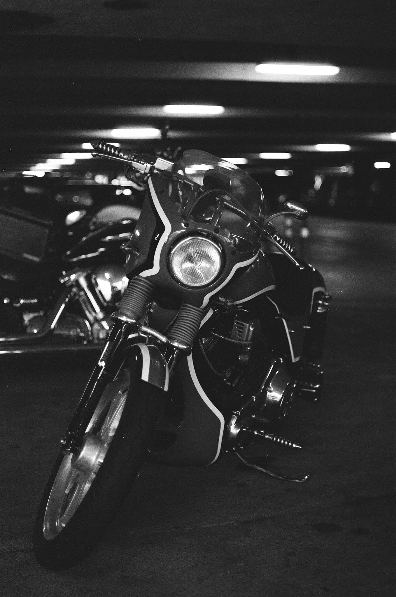 Black and white photo of a motorcycle parked in a dimly lit garage with other vehicles in the background.