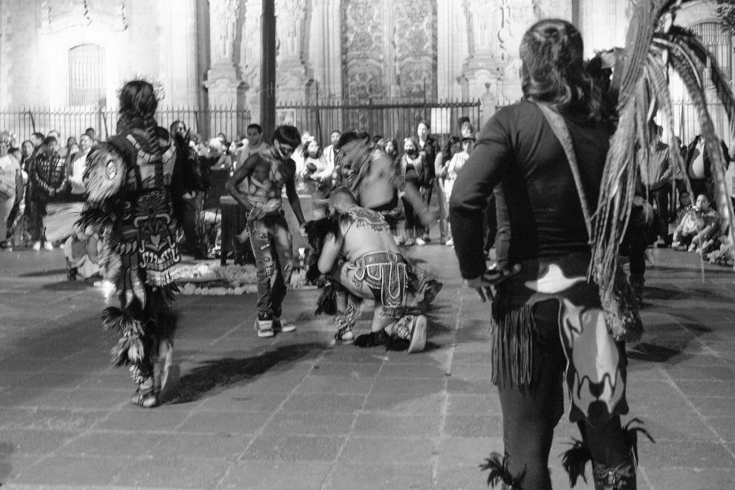 Indigenous dancers performing a traditional dance in front of an audience outdoors at night.