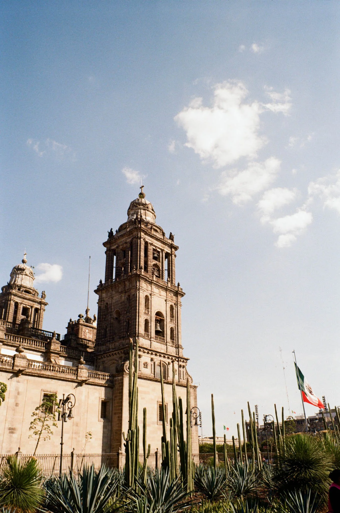 Historical church with twin towers, surrounded by desert plants and Mexican flags.