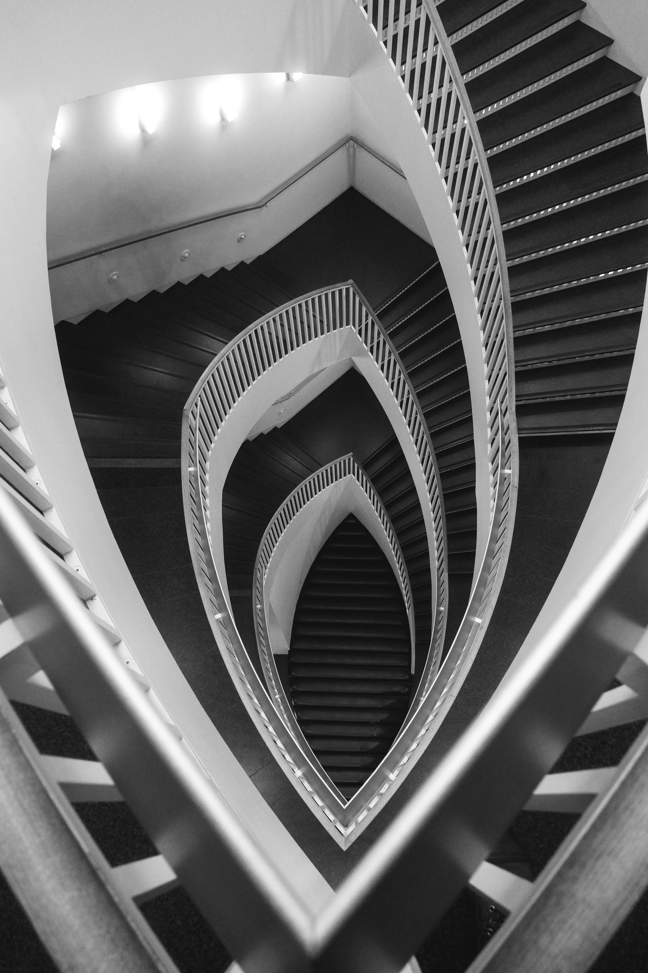 Black and white photograph of a spiraling staircase seen from above, creating a heart-shaped pattern with the steps and railings.