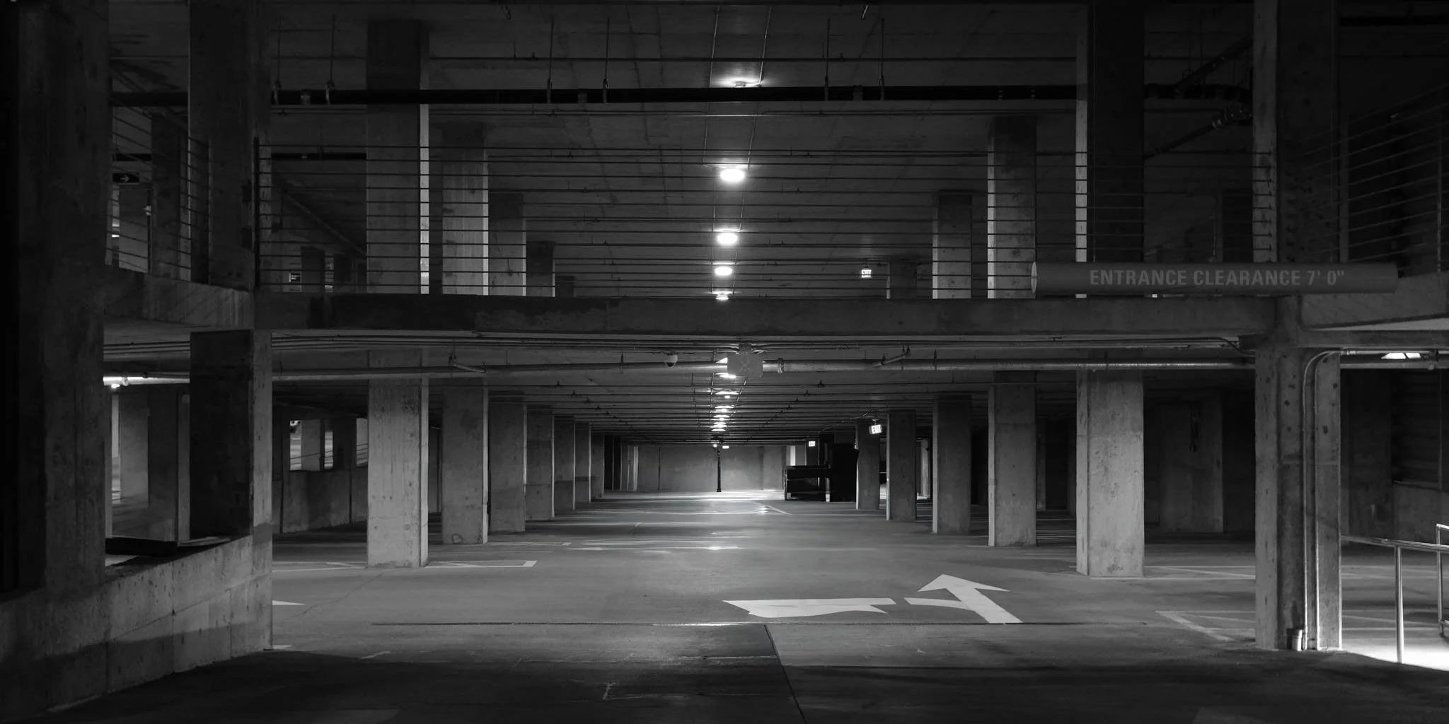 Underground parking garage with concrete columns and multiple levels, illuminated by overhead lighting, with an arrow pointing left on the floor.