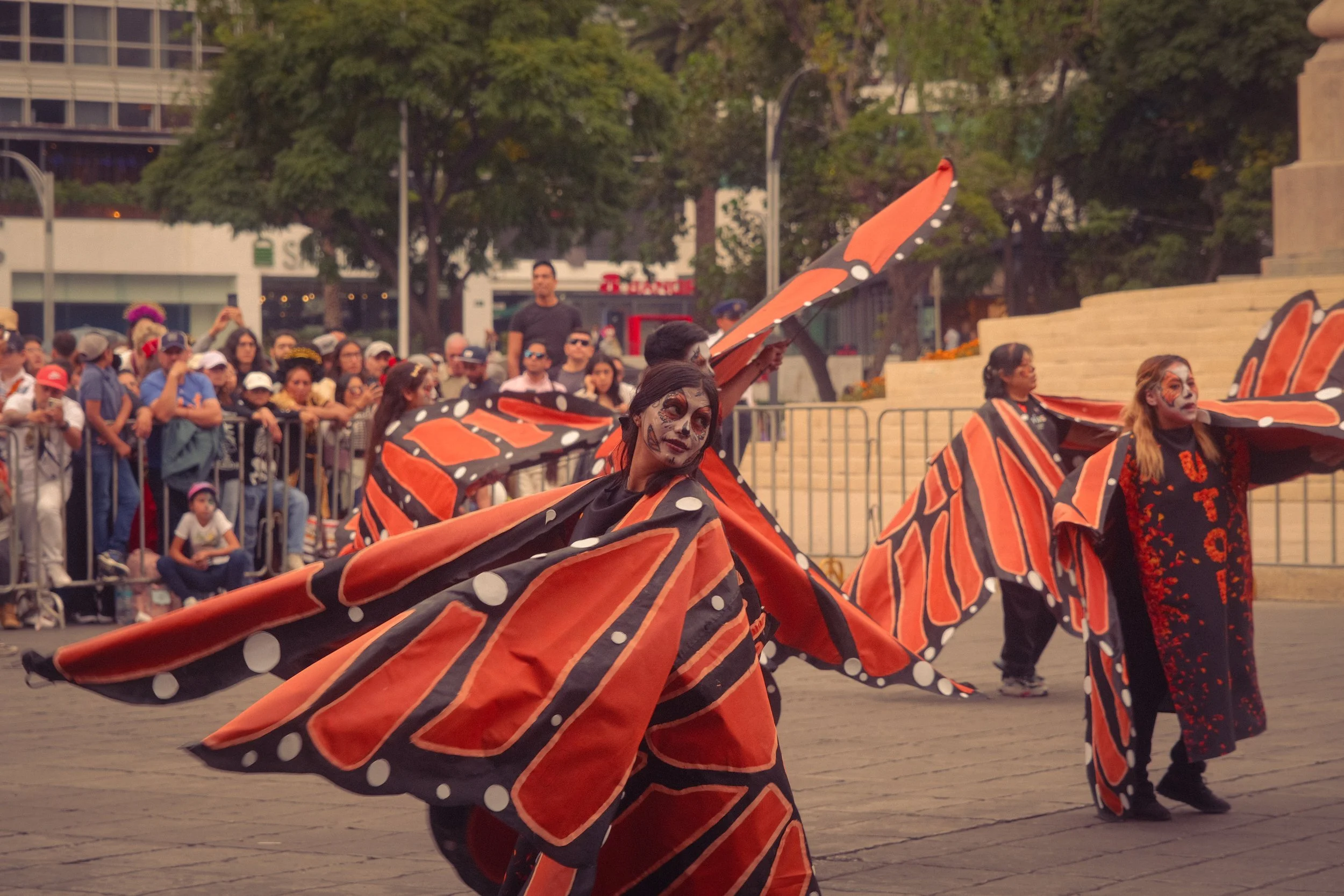 Performers dressed as butterflies with colorful wings dancing in a parade in front of a crowd of spectators.