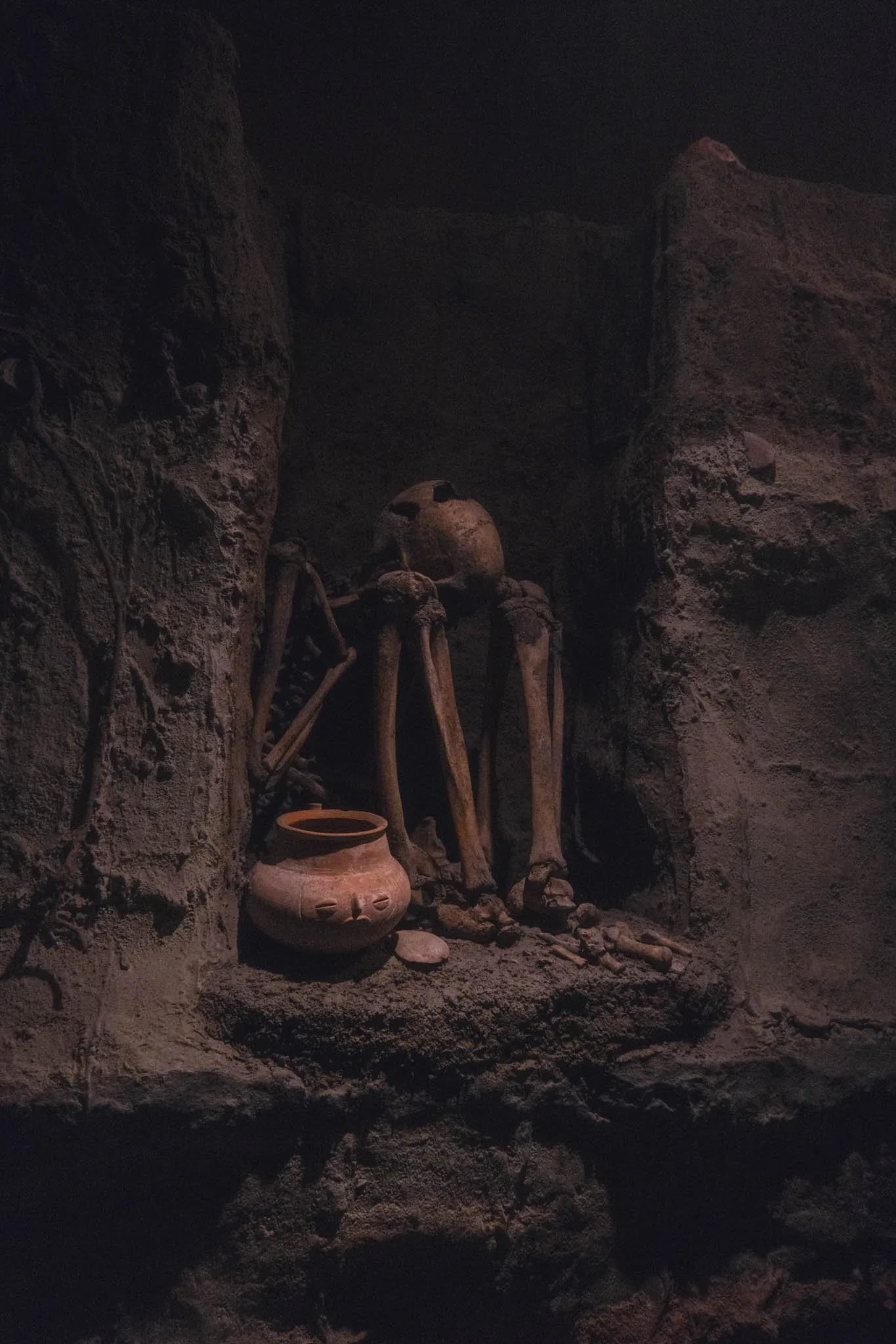 Ancient skeleton and pottery artifact within a dark stone alcove.