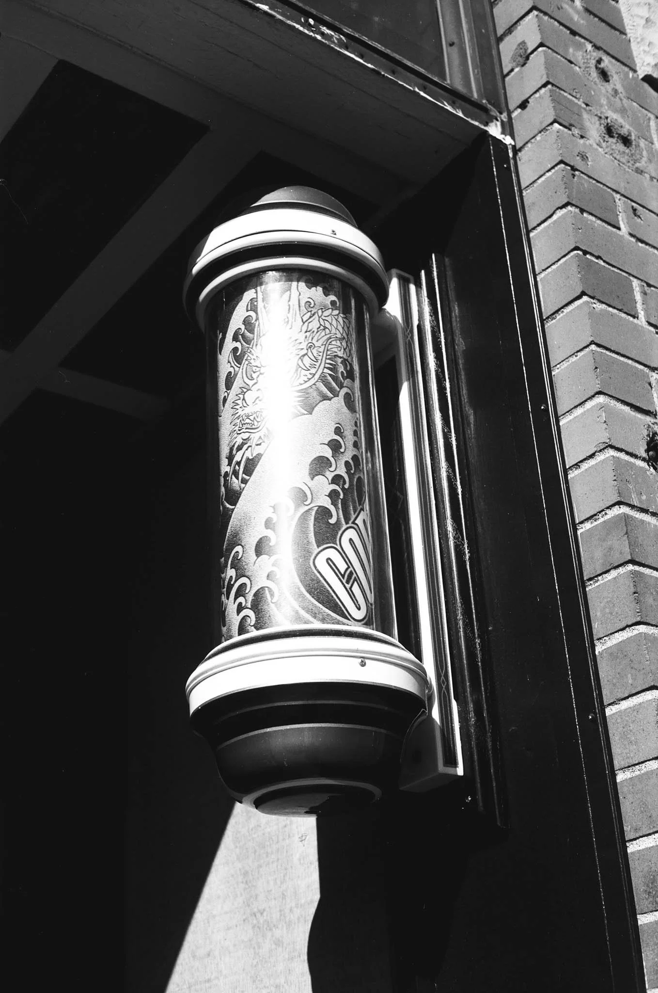 A black and white photo of a decorative street fire hydrant with a dragon design on it, mounted on a building exterior next to bricks.