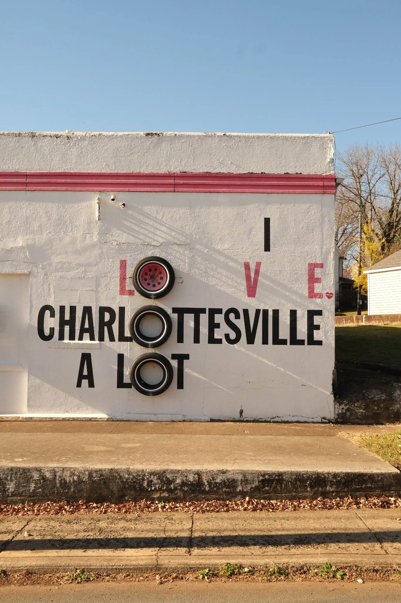 A mural on a white building wall with the message "I love Charlottesville a lot"; the letters are arranged with some words split between black and red text, and the O's in "lot" are represented by car tires.