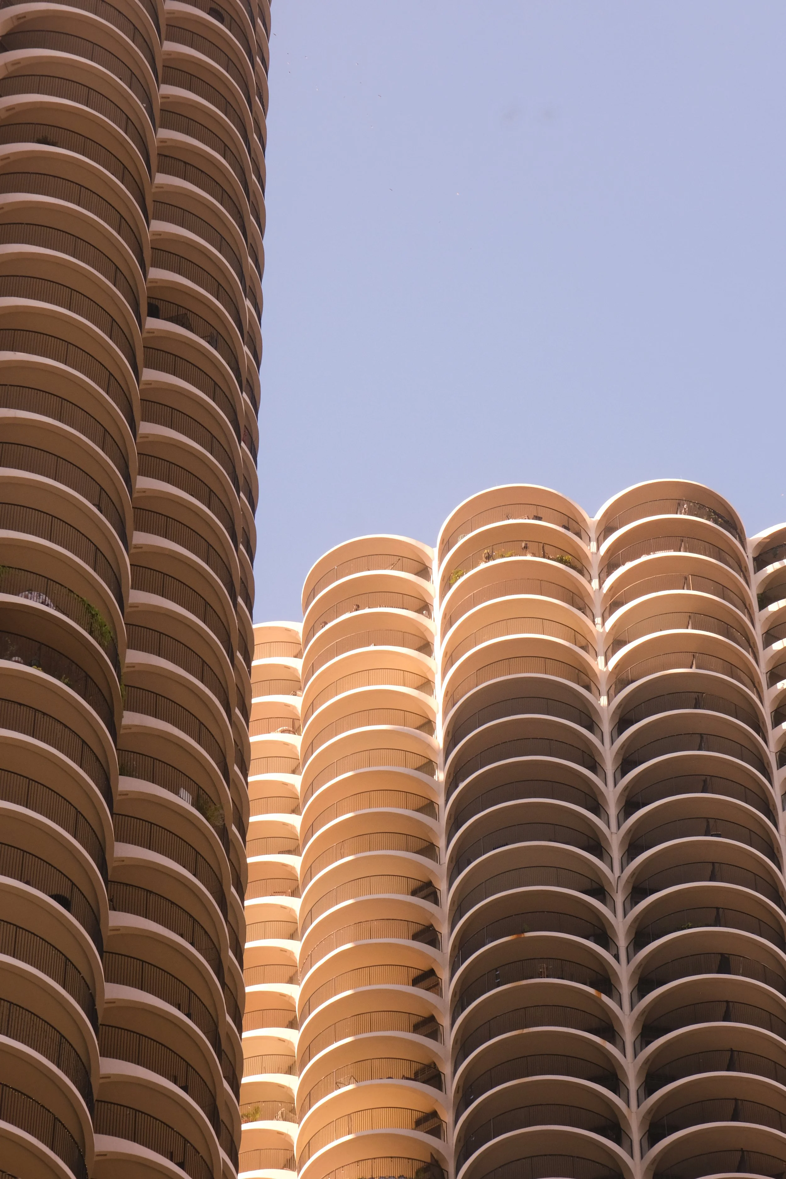 Tall modern apartment buildings with curved balconies against a clear blue sky.