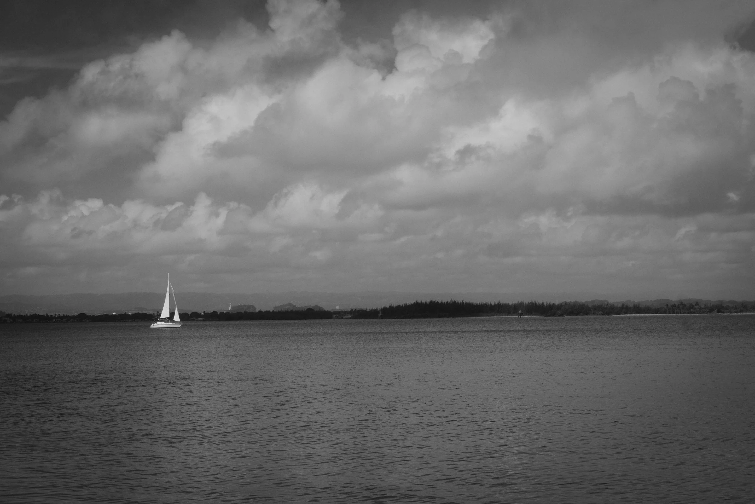 A sailboat with a white sail on a calm lake with a cloudy sky overhead.
