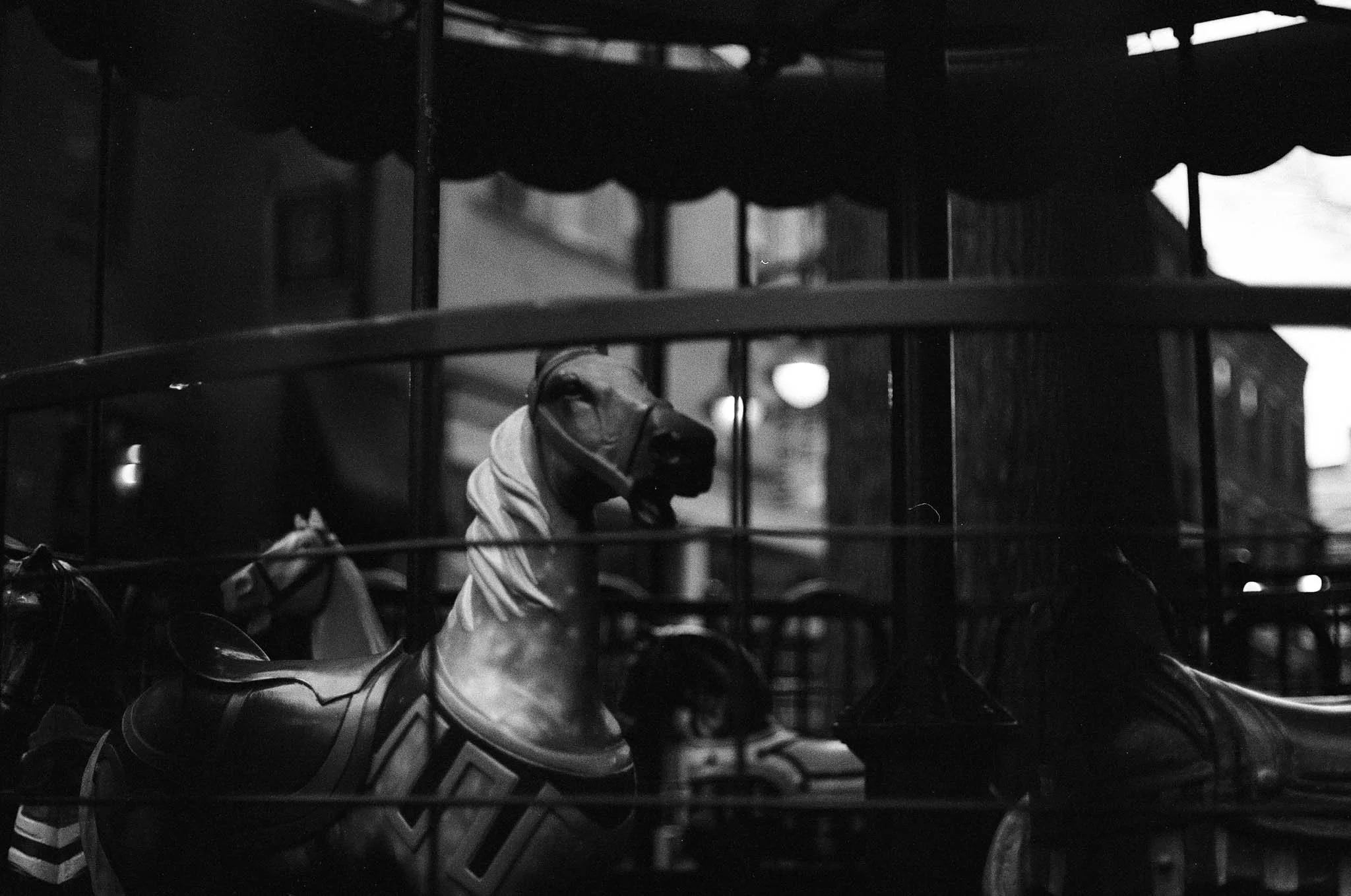 A carousel horse with a person's head and part of their face showing, wearing a hoodie and cap, on a dark street in black and white