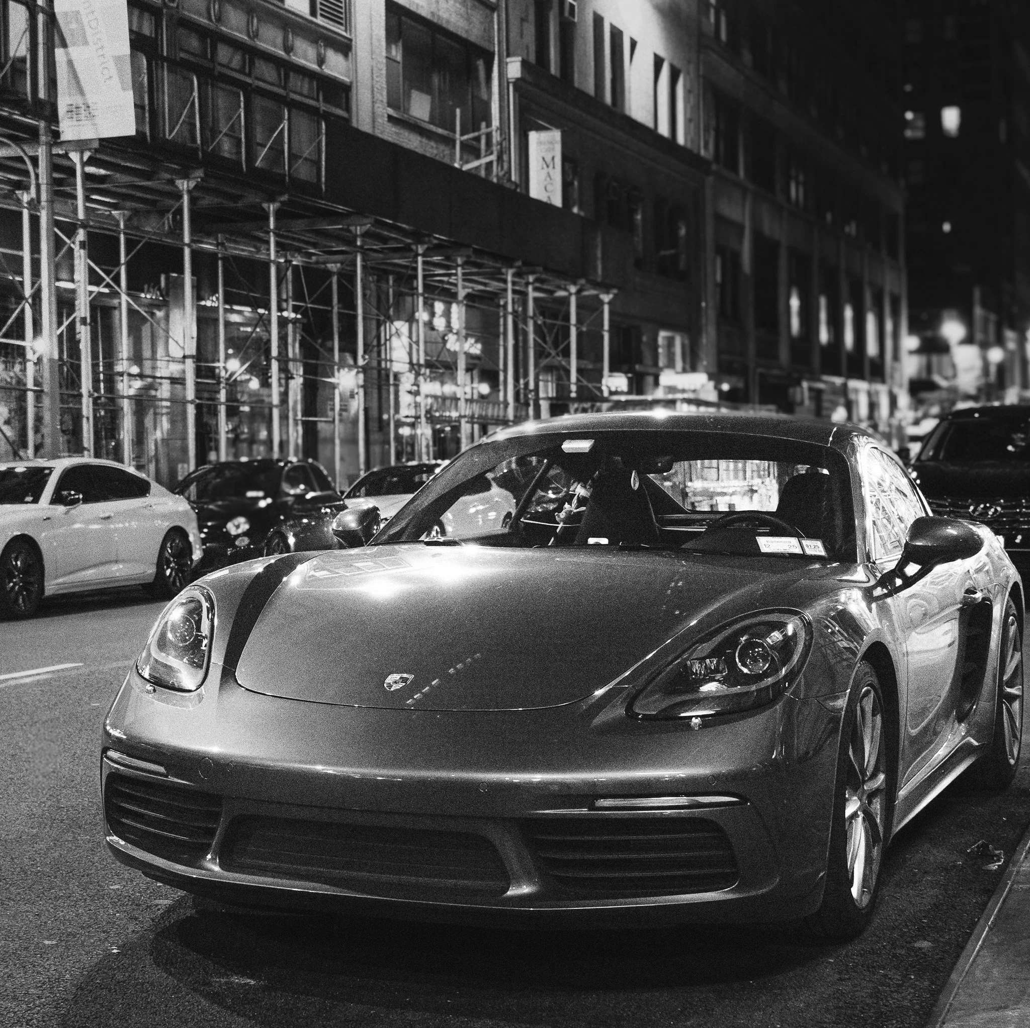 A sleek sports car parked on a city street at night, with buildings and other cars in the background.
