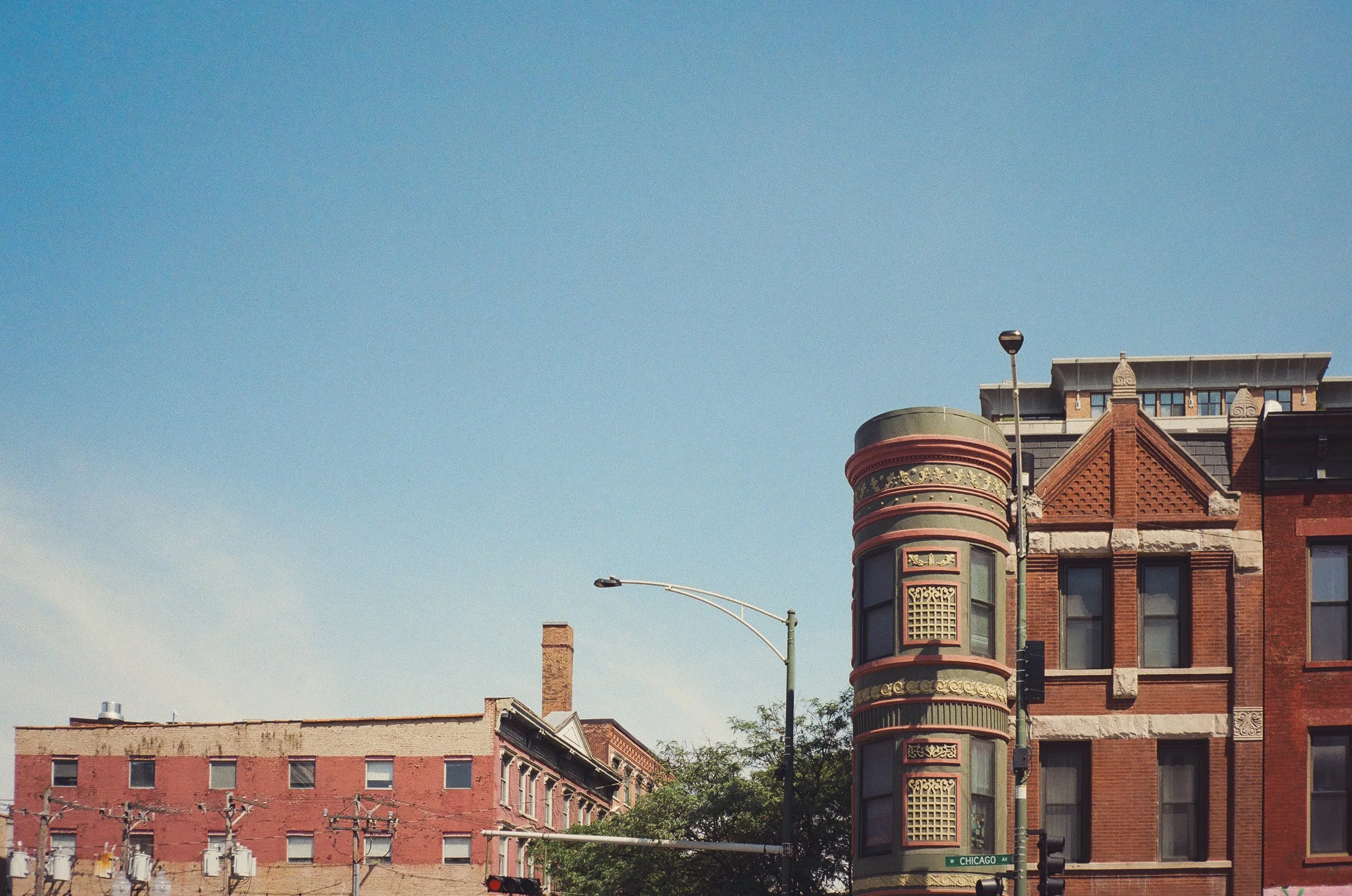Street scene in a city with historic brick buildings, streetlights, power lines, and a clear blue sky, with a sign indicating Chicago Avenue.