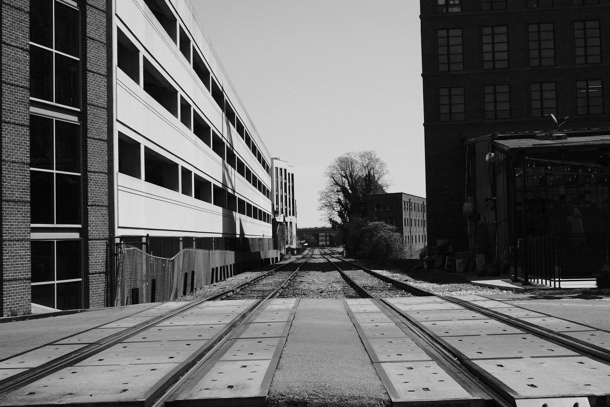 Black and white photo of train tracks extending through an urban area with modern and older buildings on either side.
