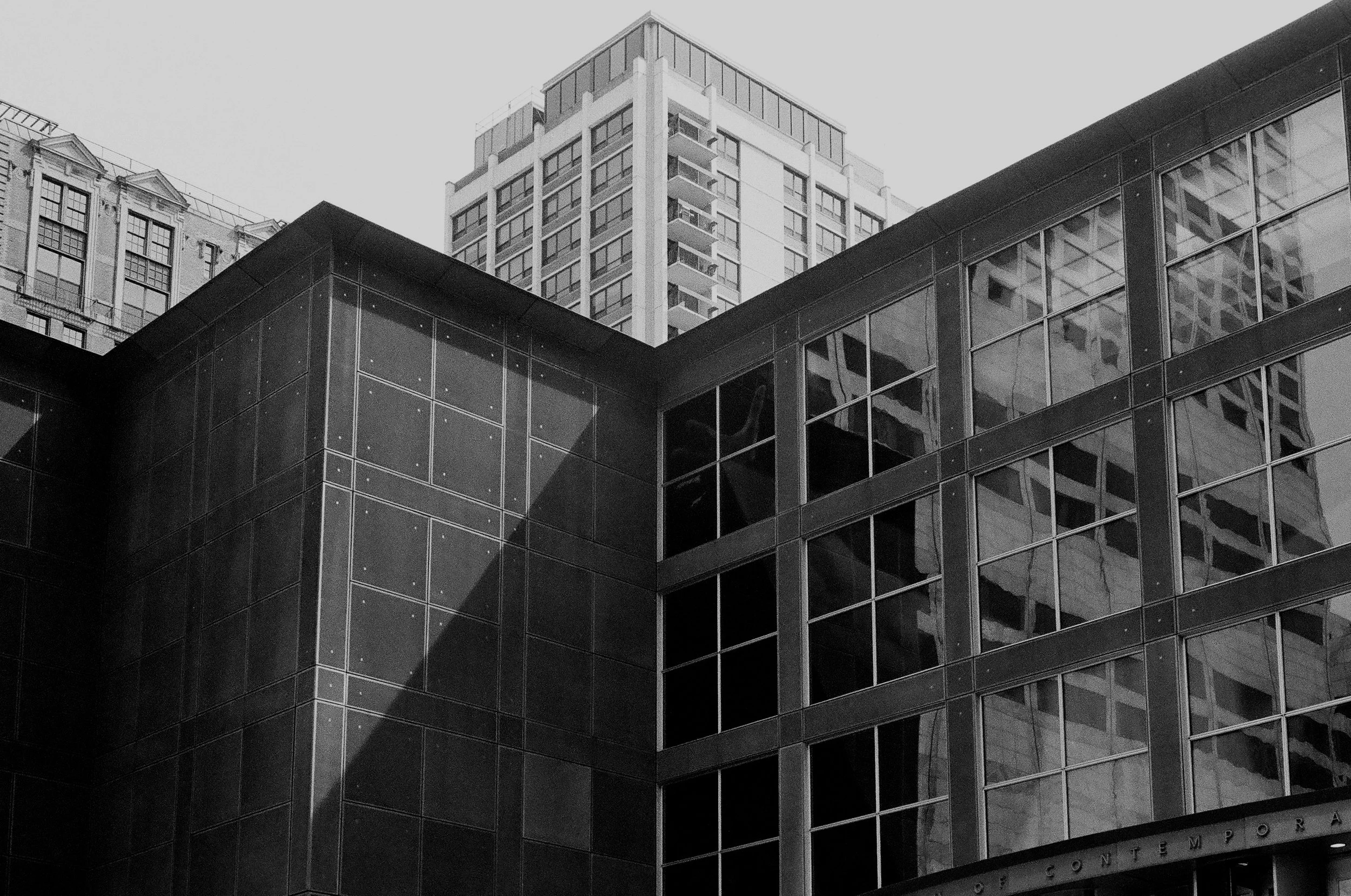 Black and white photograph of modern glass and metal building with high-rise buildings in the background.
