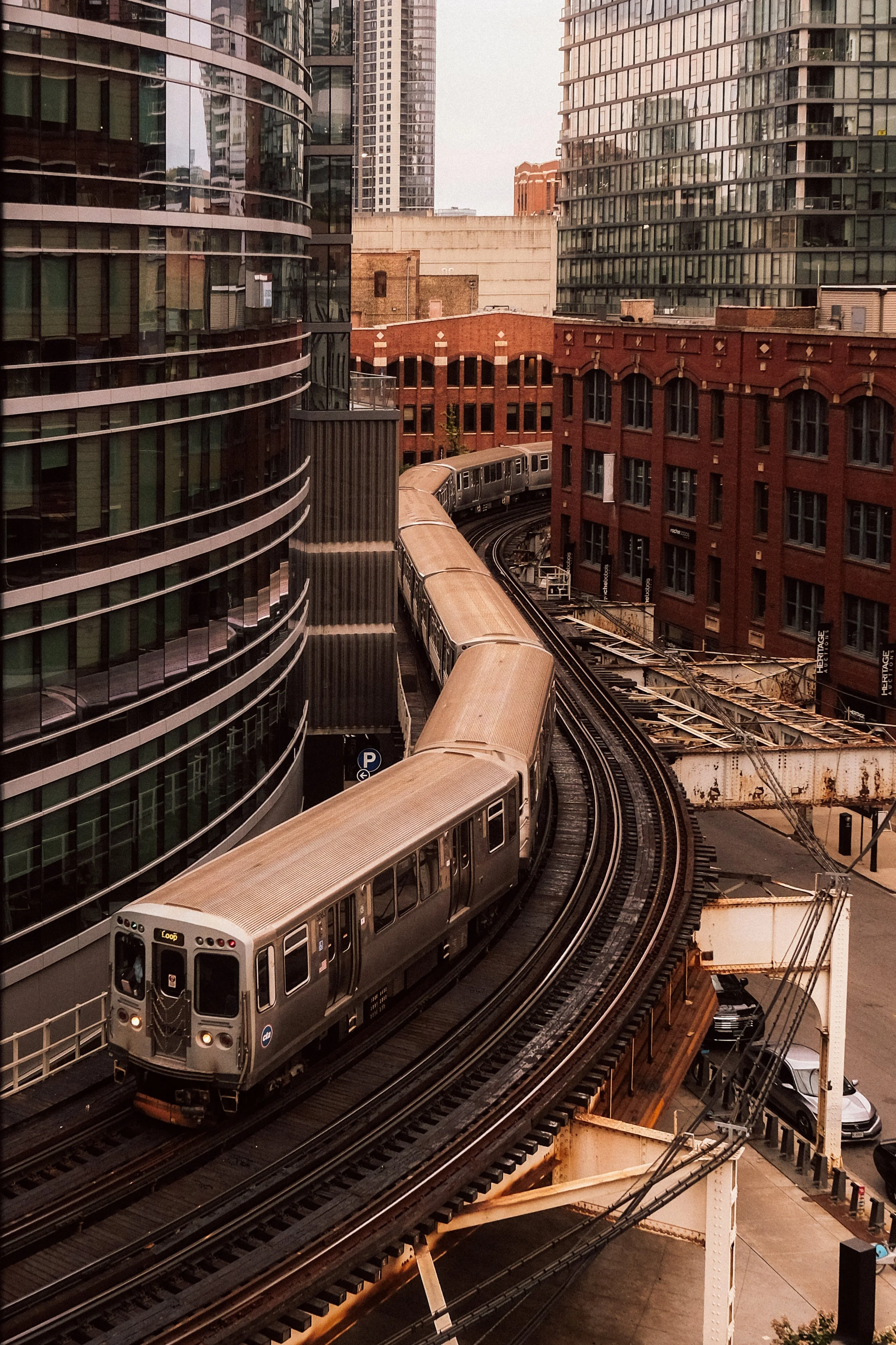 An elevated train traveling through a city with tall modern glass buildings and older brick buildings around the tracks.