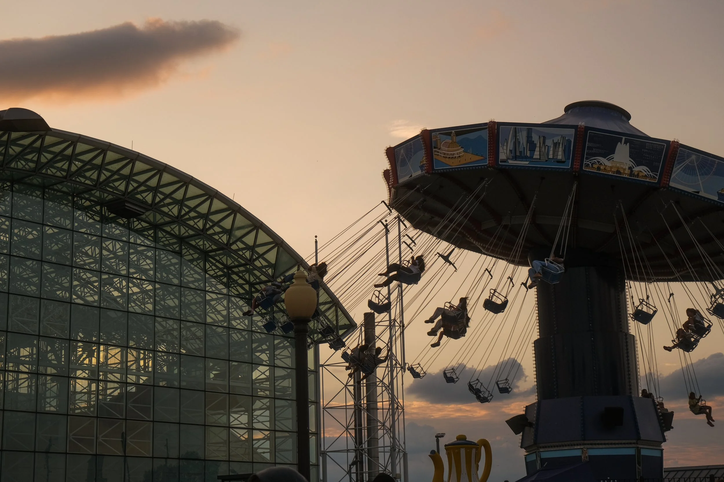 People riding on a swing amusement ride at sunset outside a modern glass building.