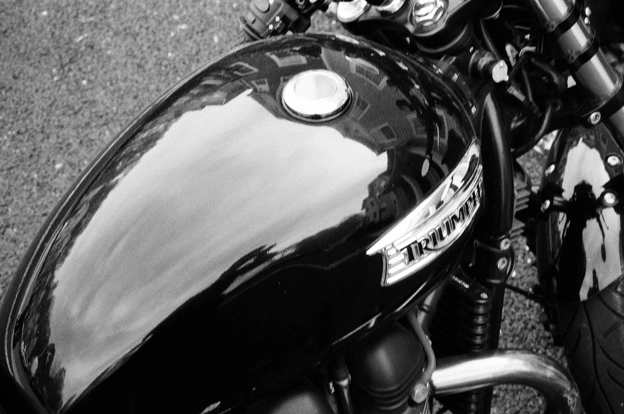 Black Triumph motorcycle fuel tank with reflection of buildings and sky.