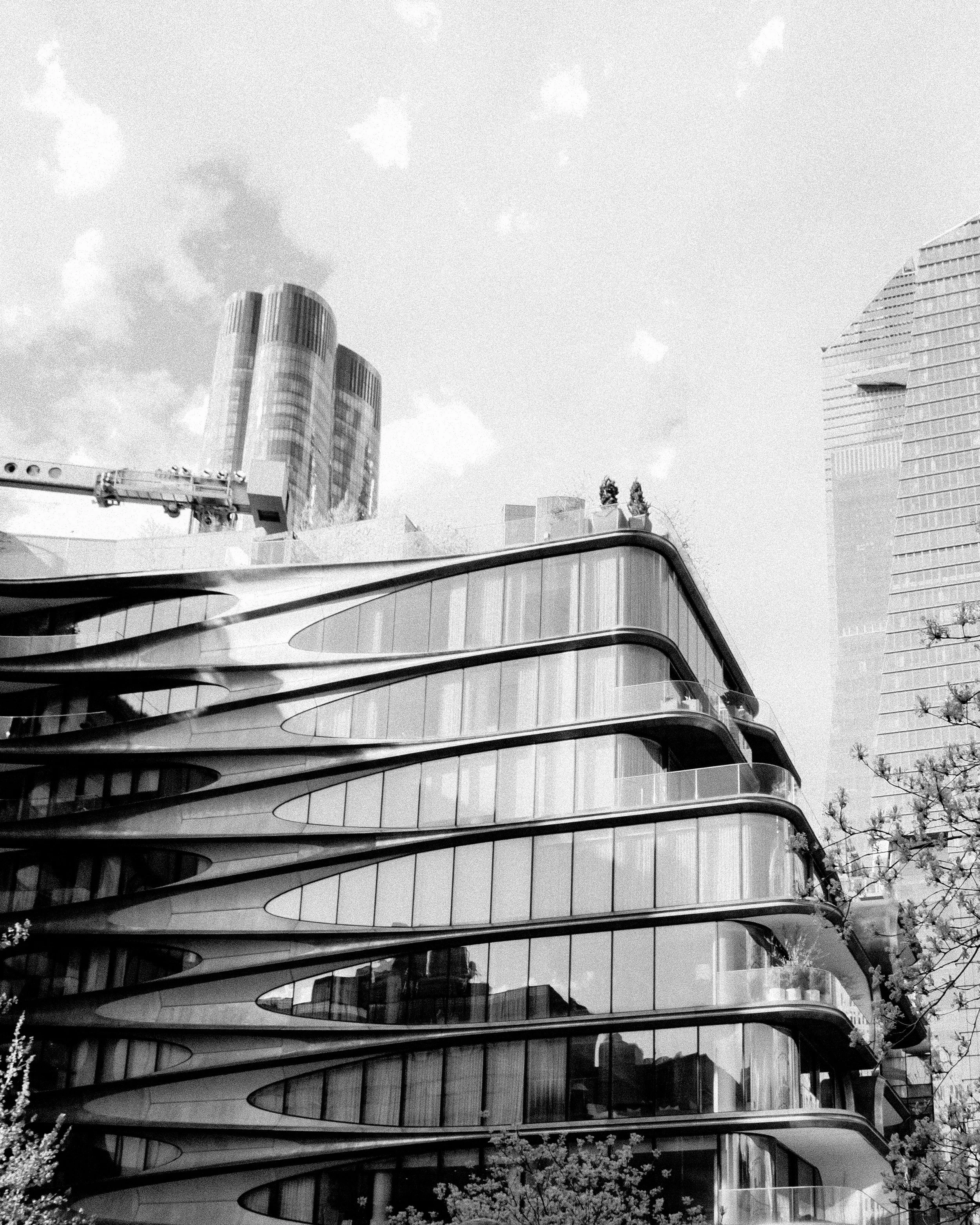 Black and white photo of modern, curvy glass building with rounded balconies in an urban cityscape.