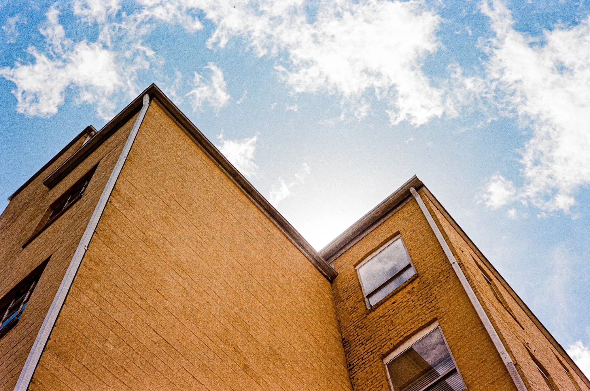View of the corner of a yellow brick building against a blue sky with scattered clouds.