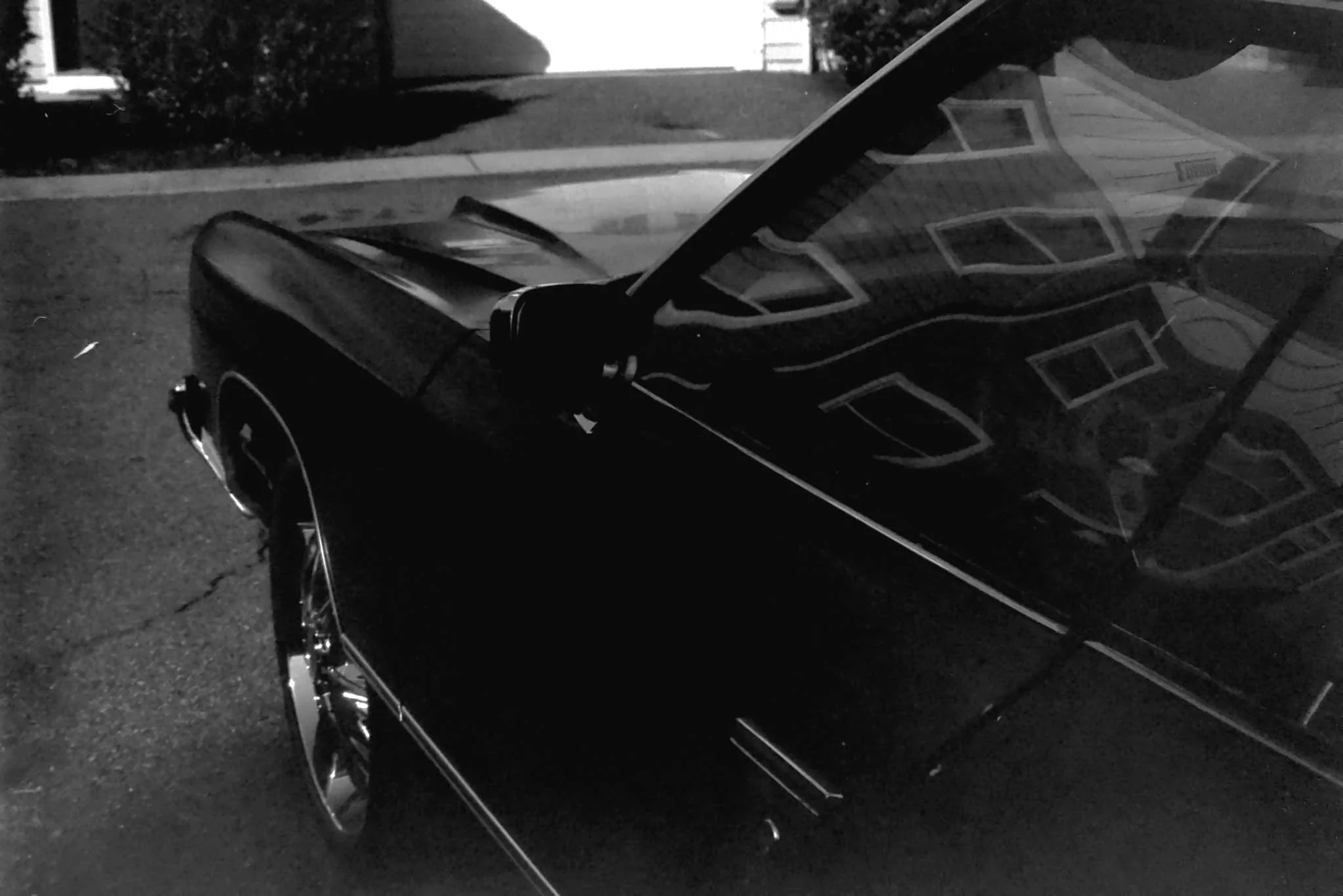Black classic car parked on a driveway at night, with reflections of house windows visible on the car's surface.