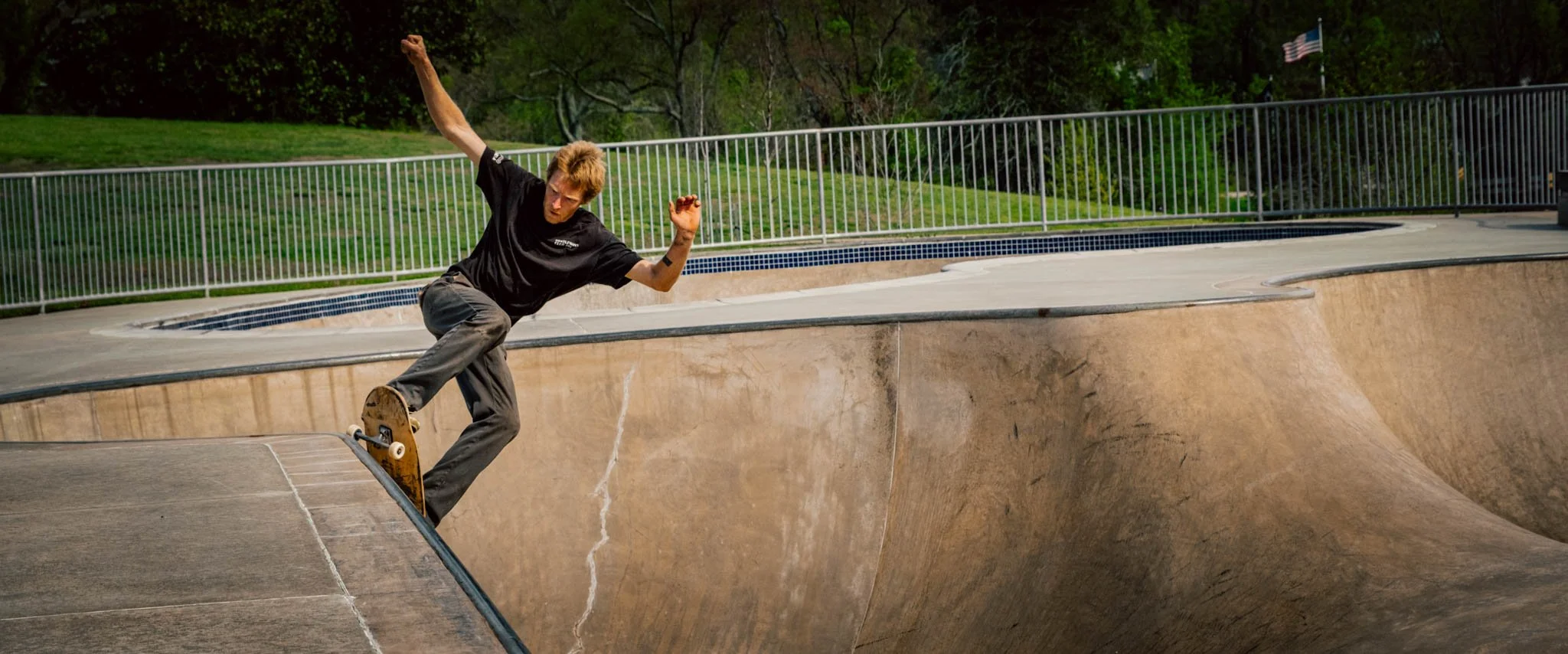 Skateboarder in black shirt and gray pants performing a trick in a concrete skate park bowl