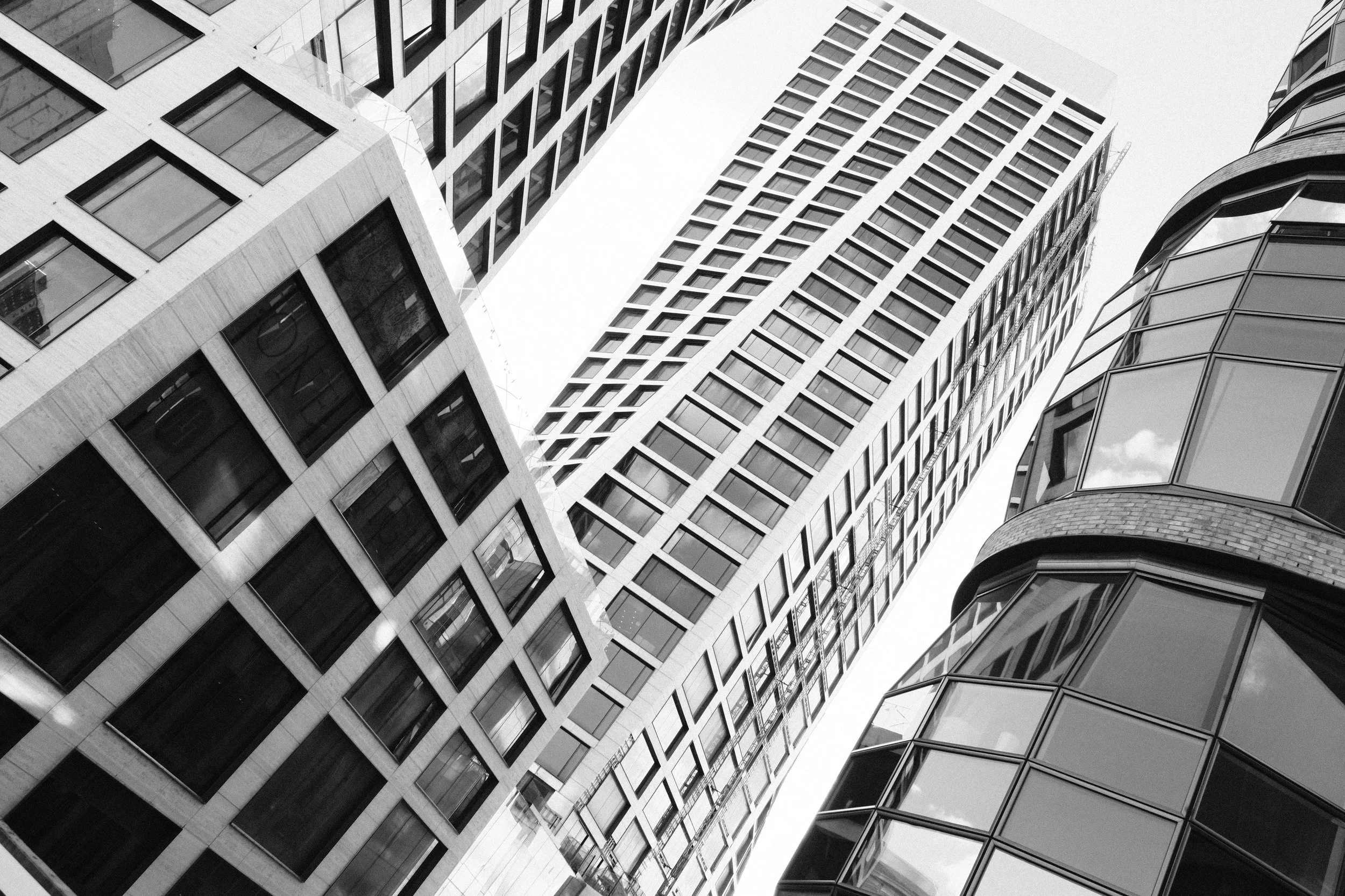Black and white photo of three modern high-rise buildings viewed from below, showcasing glass windows and geometric architectural designs.
