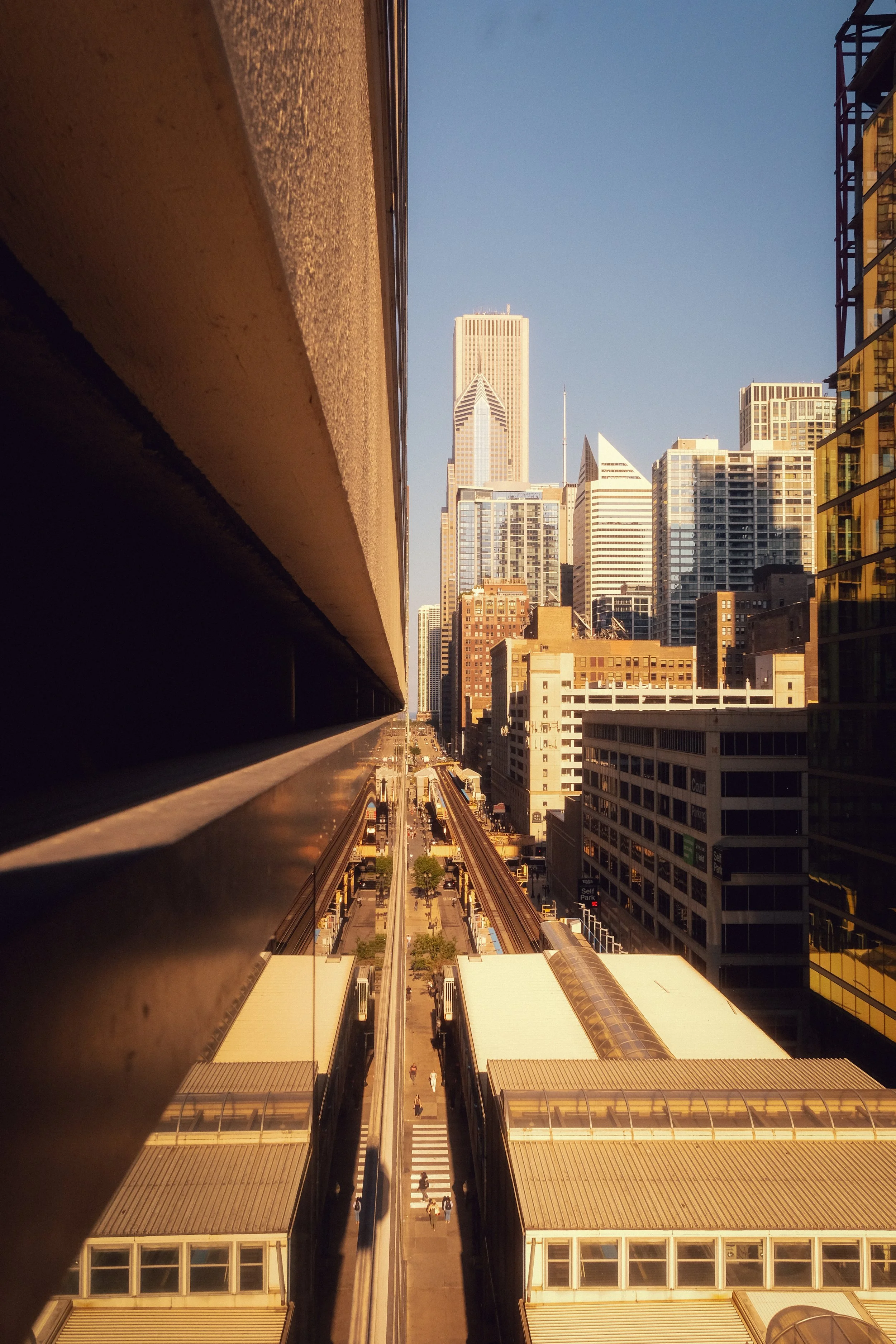 Cityscape view from a high vantage point showing skyscrapers, a train station, railway tracks, and sidewalks in an urban area.
