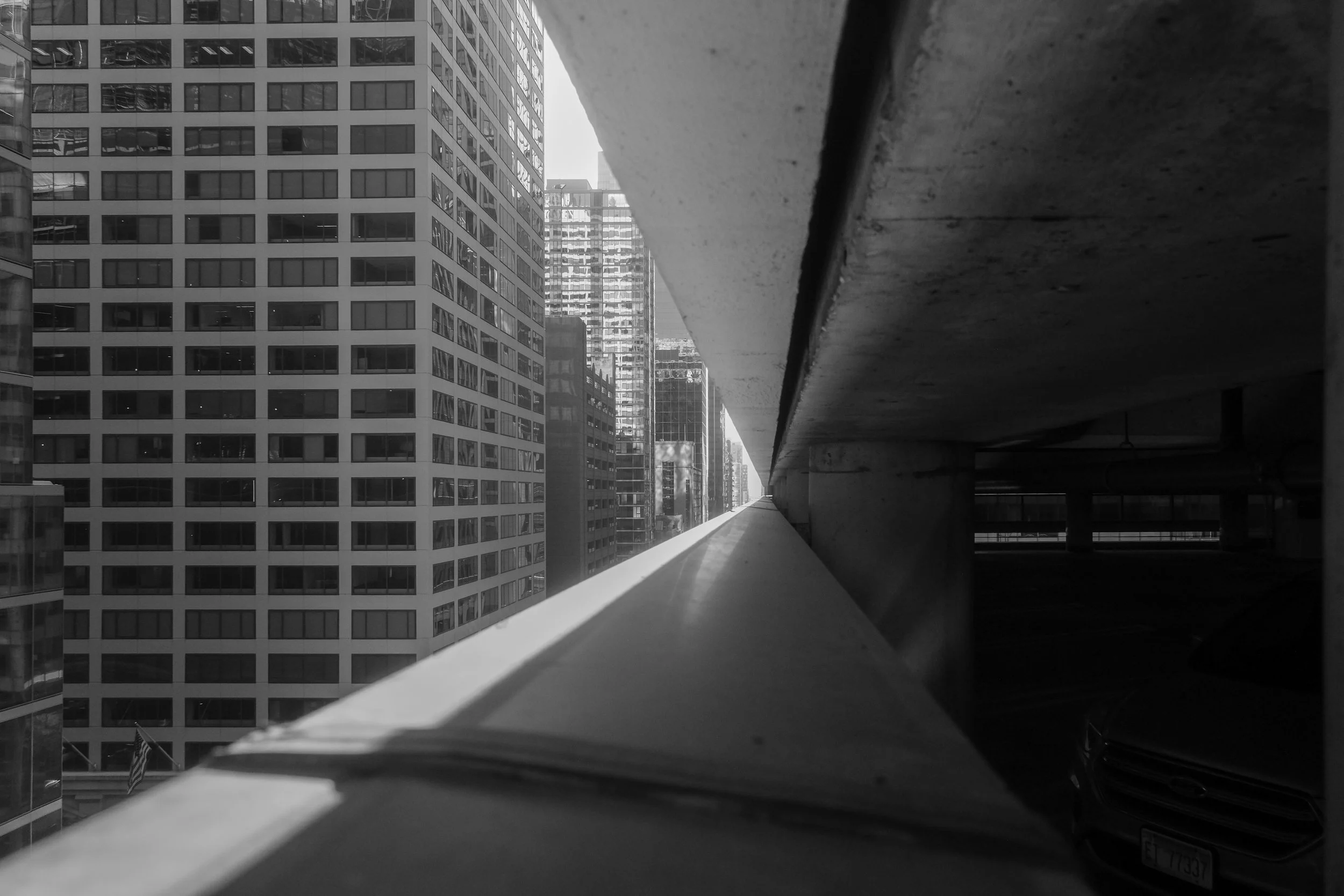View of city skyscrapers taken from a balcony or ledge, with part of the building's structure on the right, in black and white.