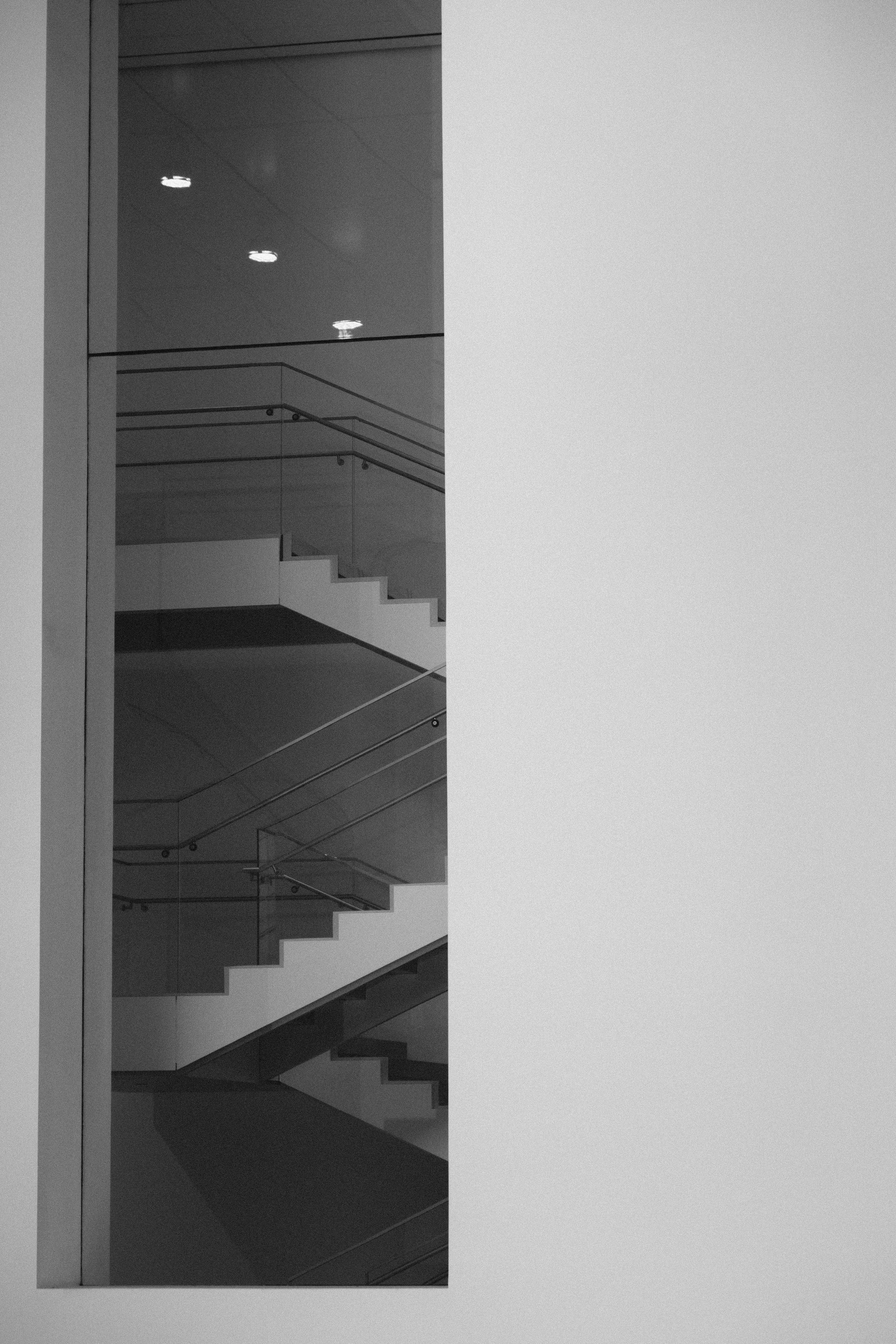 A black and white photo of an indoor staircase with multiple landings and railings, viewed through a glass wall in a modern building.