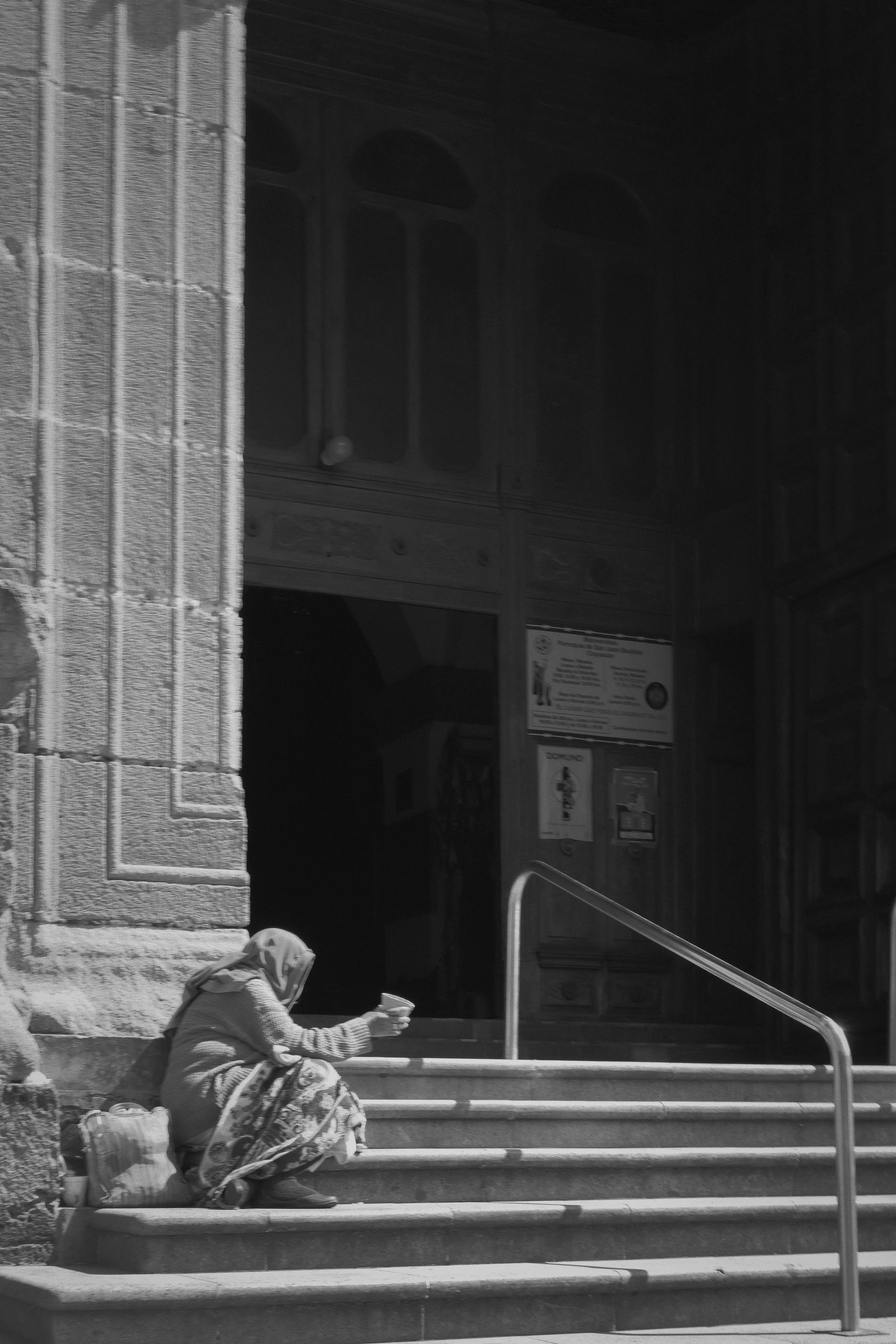 A woman sitting on the stairs outside a large stone building, reading a piece of paper or a book.