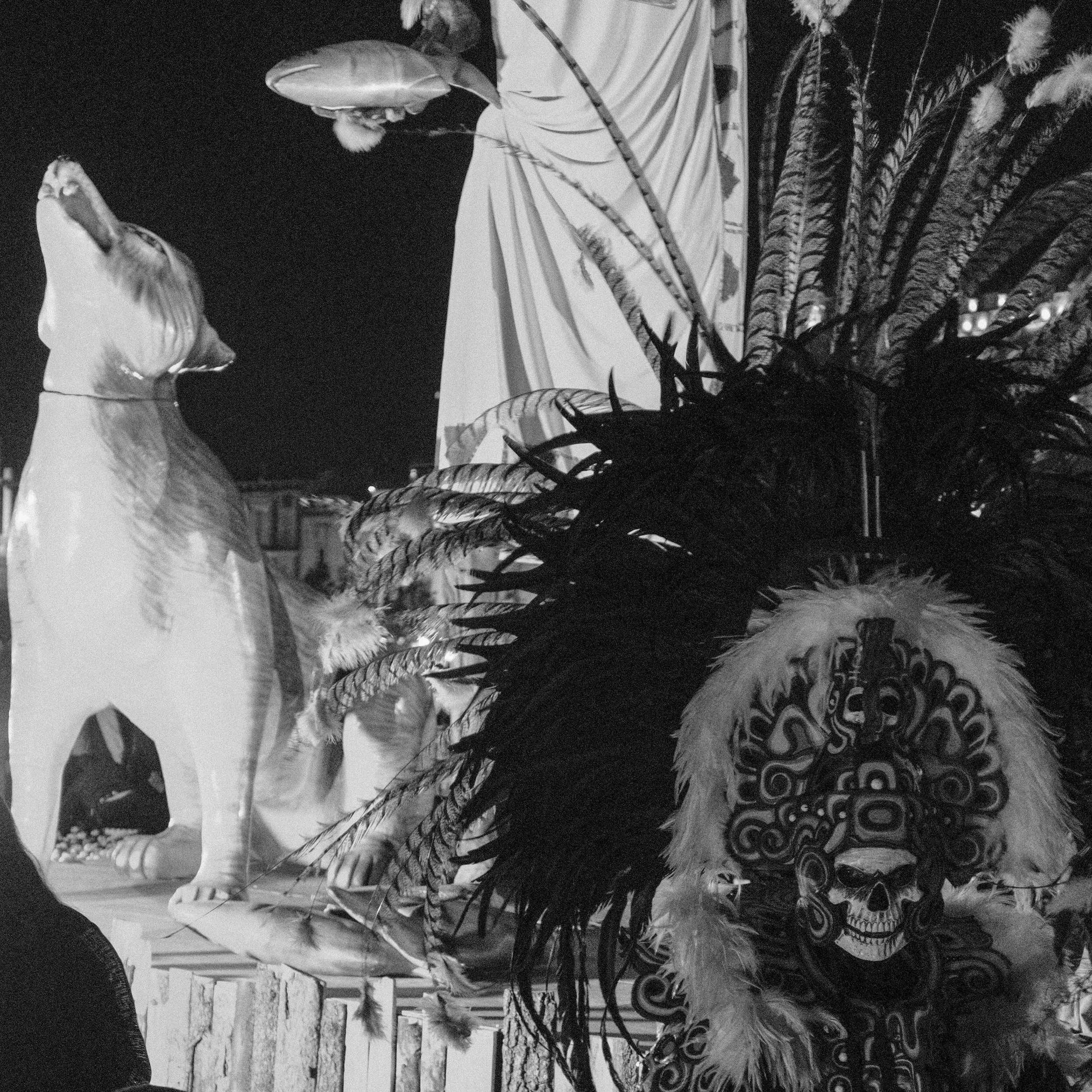A display with a large feathered headdress featuring a skull design, an inflatable horse figure, and a flag with wild animal print, set against a night sky.