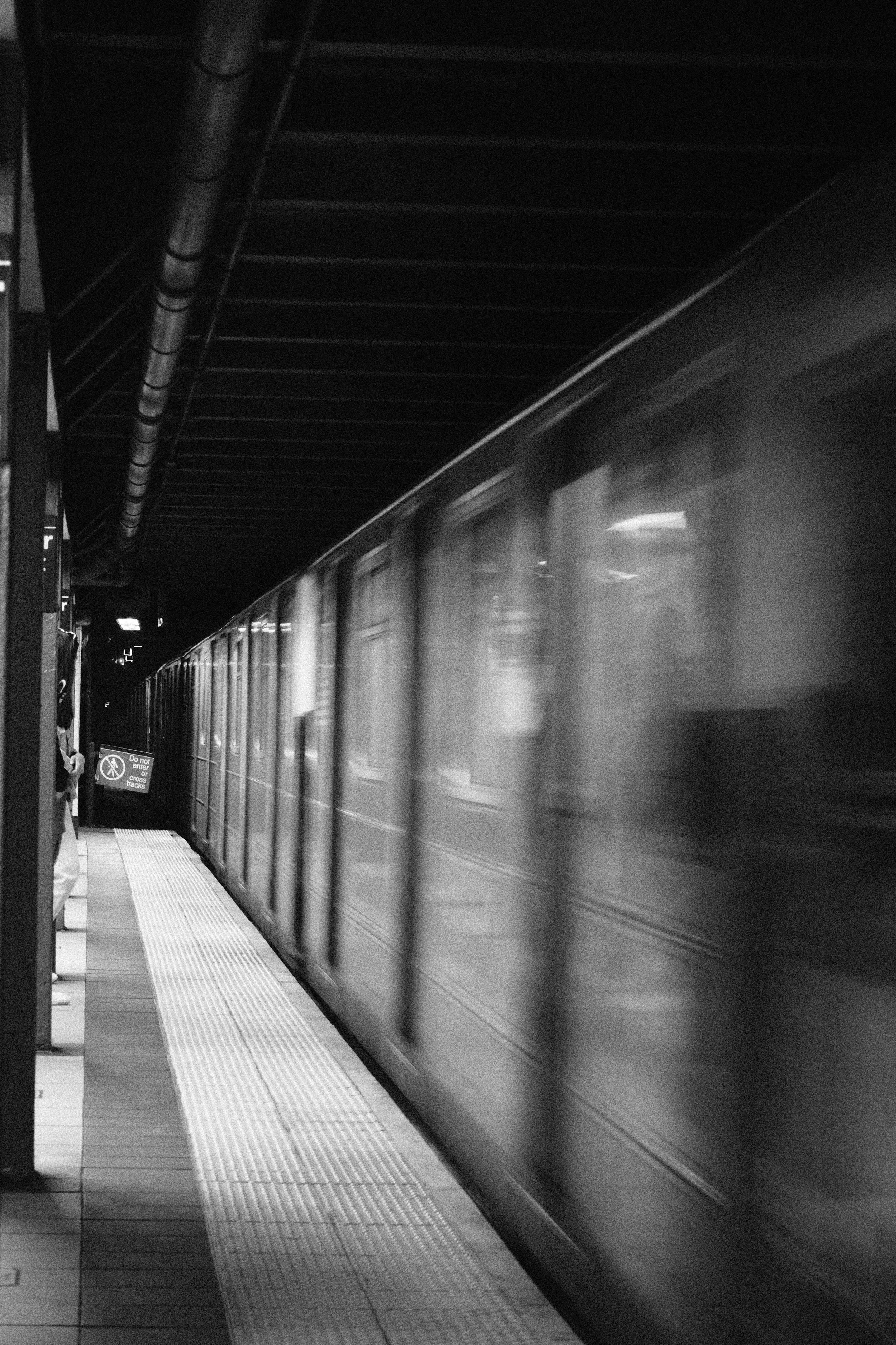 A subway train arriving at an underground station, captured in black and white, with motion blur indicating movement.