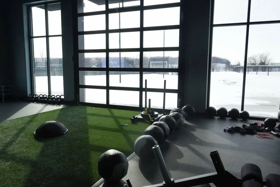 Indoor gym with kettlebells, a plyo box, and resistance bands near large windows showing snow outside.