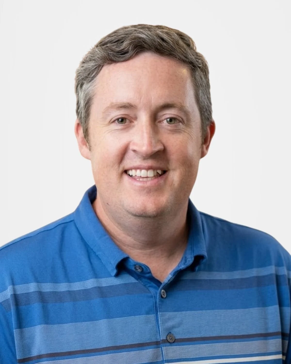 A man with short, light brown hair smiling, wearing a blue striped polo shirt, against a plain white background.
