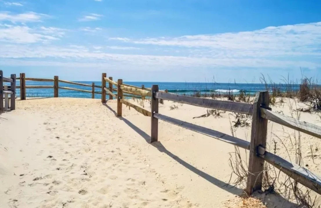 A sandy beach with wooden fences and the ocean in the background under a partly cloudy sky.