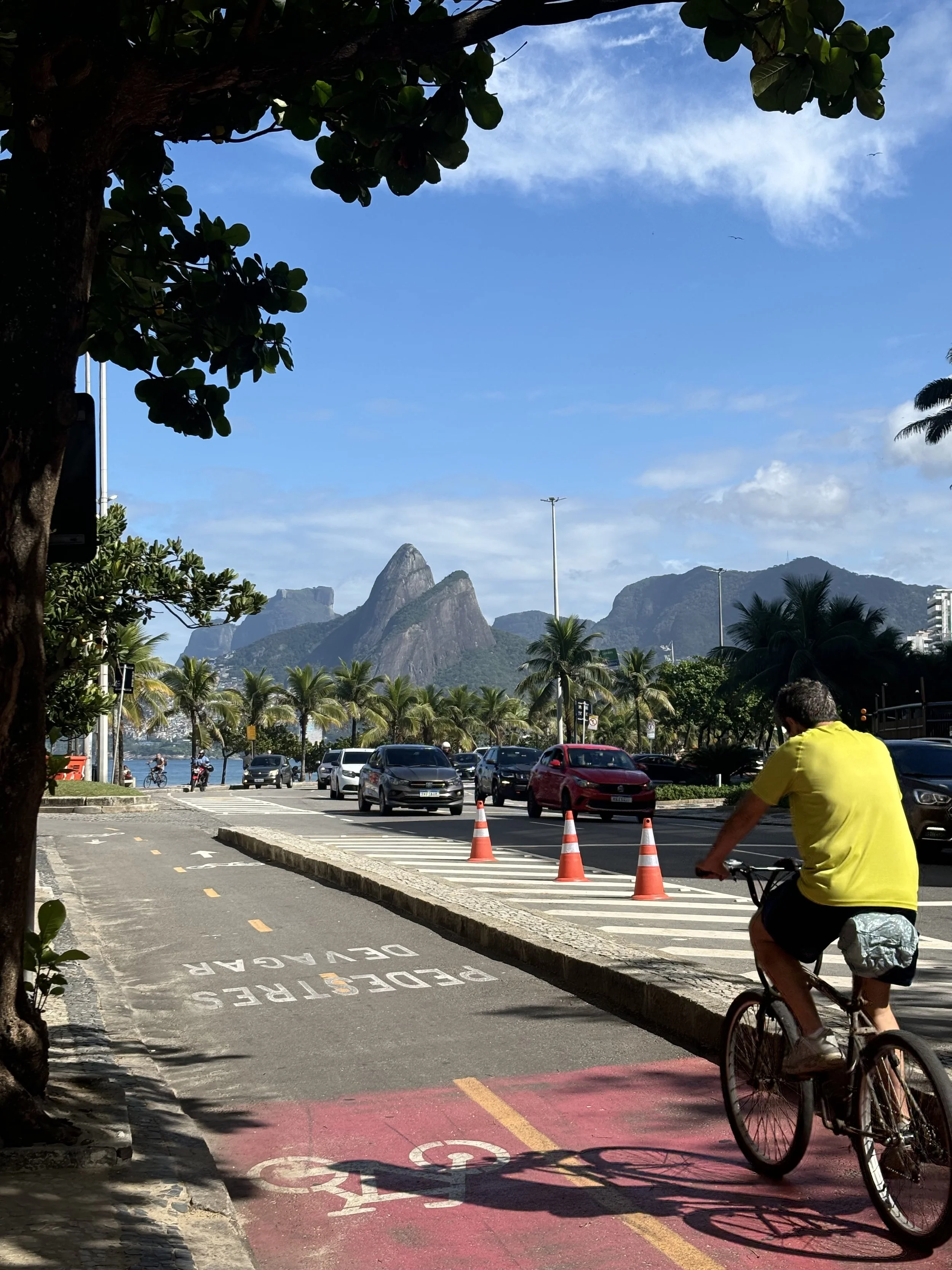 Ipanema, Rio de Janeiro — The city doesn't pause for the sea. A single figure cuts through the coastal rhythm in ordinary choreography, where the density of urban life dissolves into palm and tide. This is Brazil in motion: unhurried yet relentless, 
