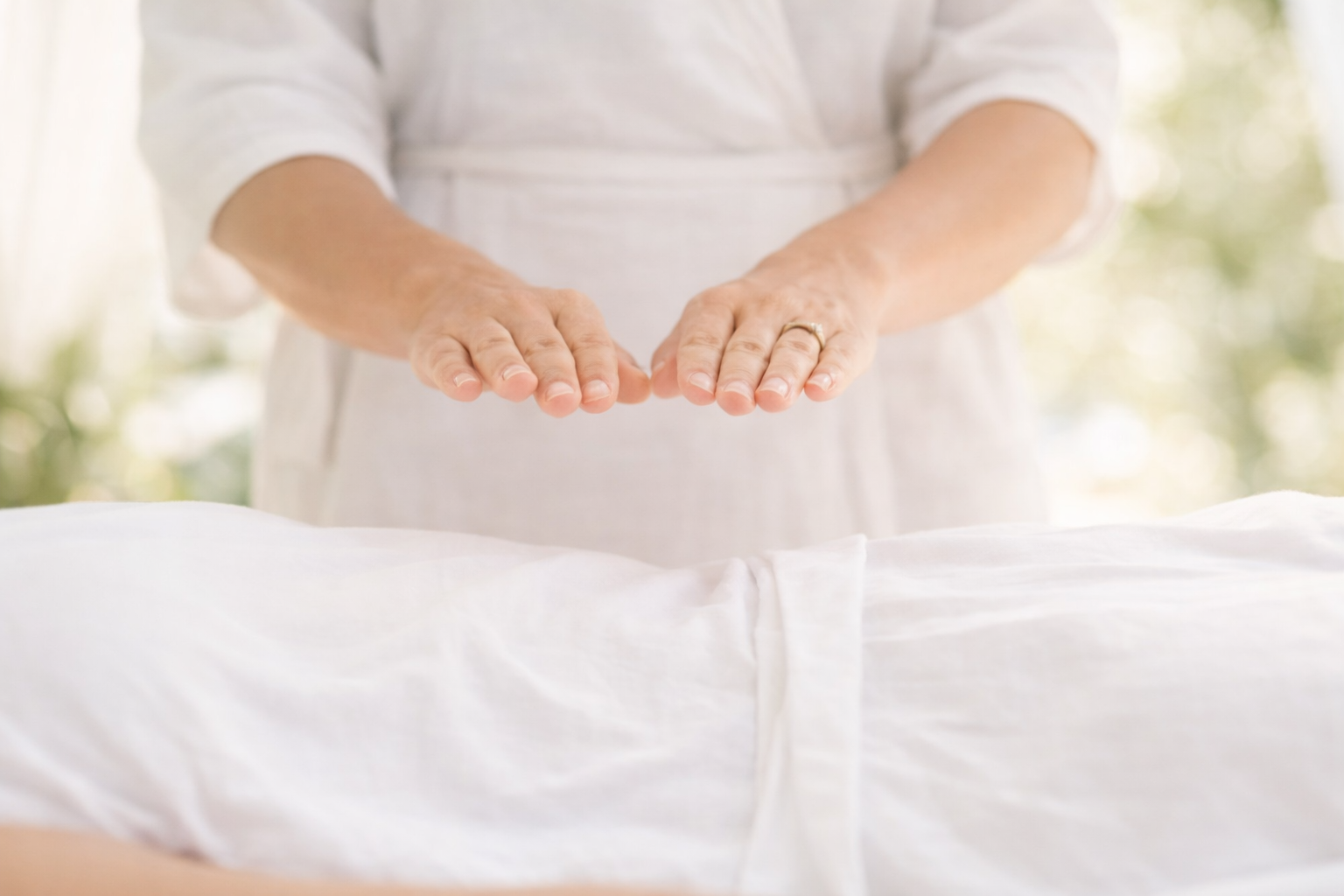 Person with hands performing a reiki healing touch or massage on a patient lying down.