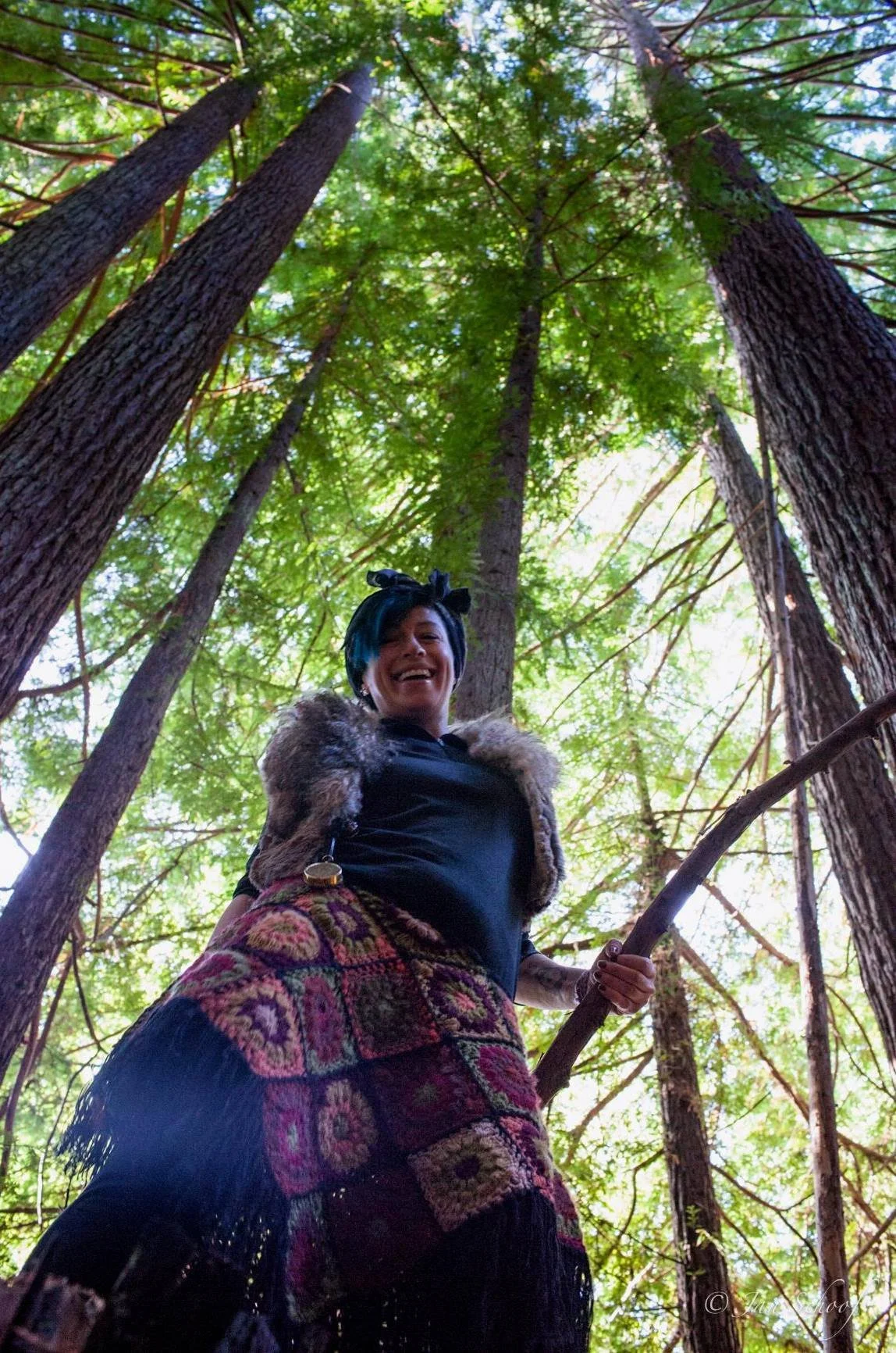 Slava standing in the Boreal forest, surrounded by lush trees. She's wearing a fur vest and crocheted skirt.