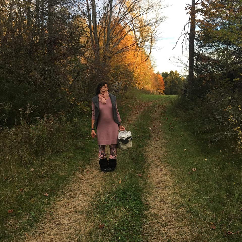 Slava, earth & body-based gestalt psychotherapist in an Ontario forest. She's out foraging for mushrooms, holding a basket. The trees are vibrant with fall colors in the background.