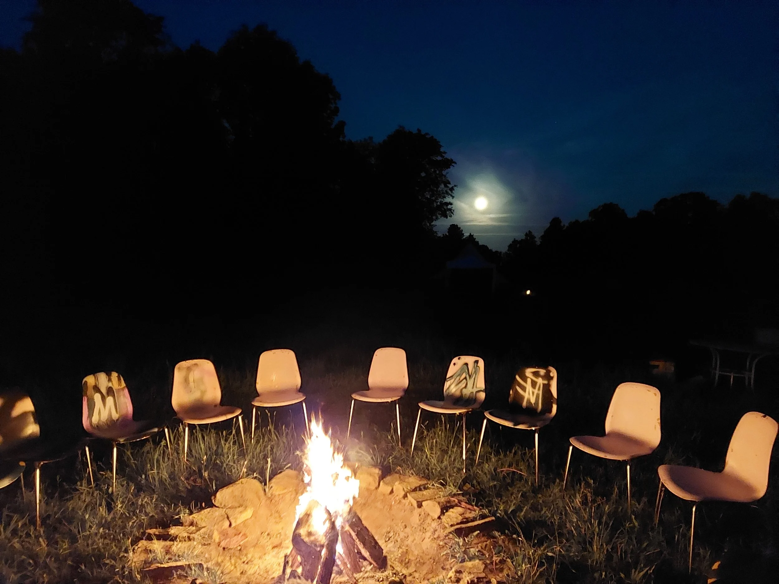Land-based retreats for groups on the land in Ontario. A circle of chairs around a fire under the full moon.