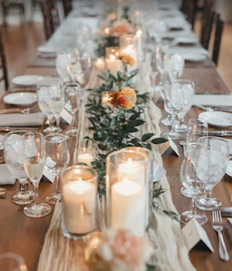 A long dining table decorated with candles, flowers, and glassware for a formal event or celebration.